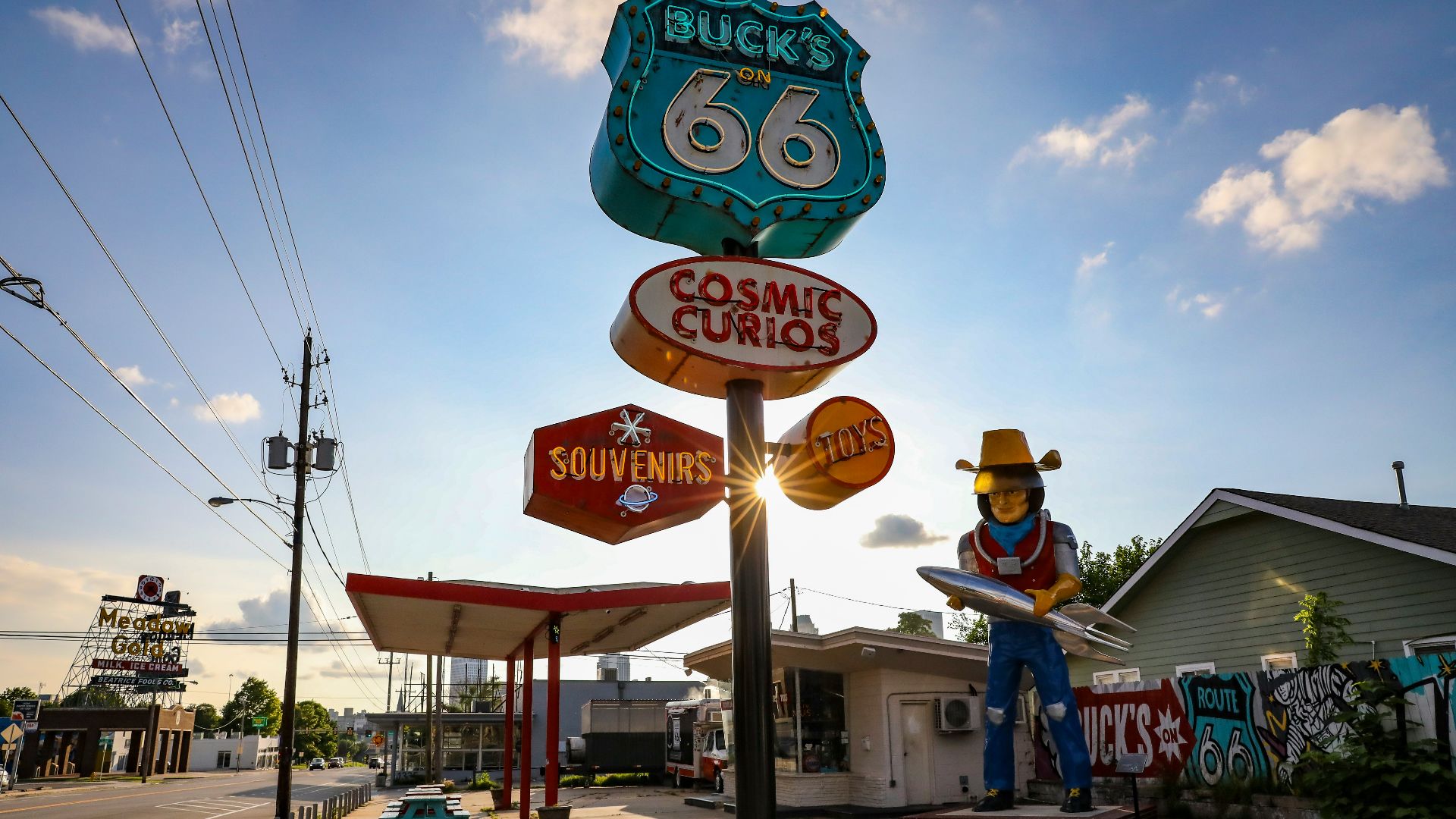 a statue of a cowboy holding a surfboard in front of a gas station