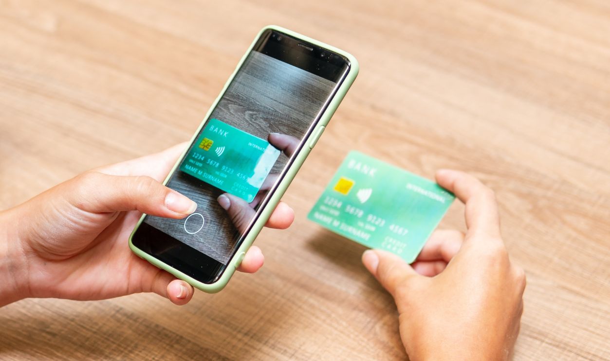 detail of woman photographing credit card with mobile at table