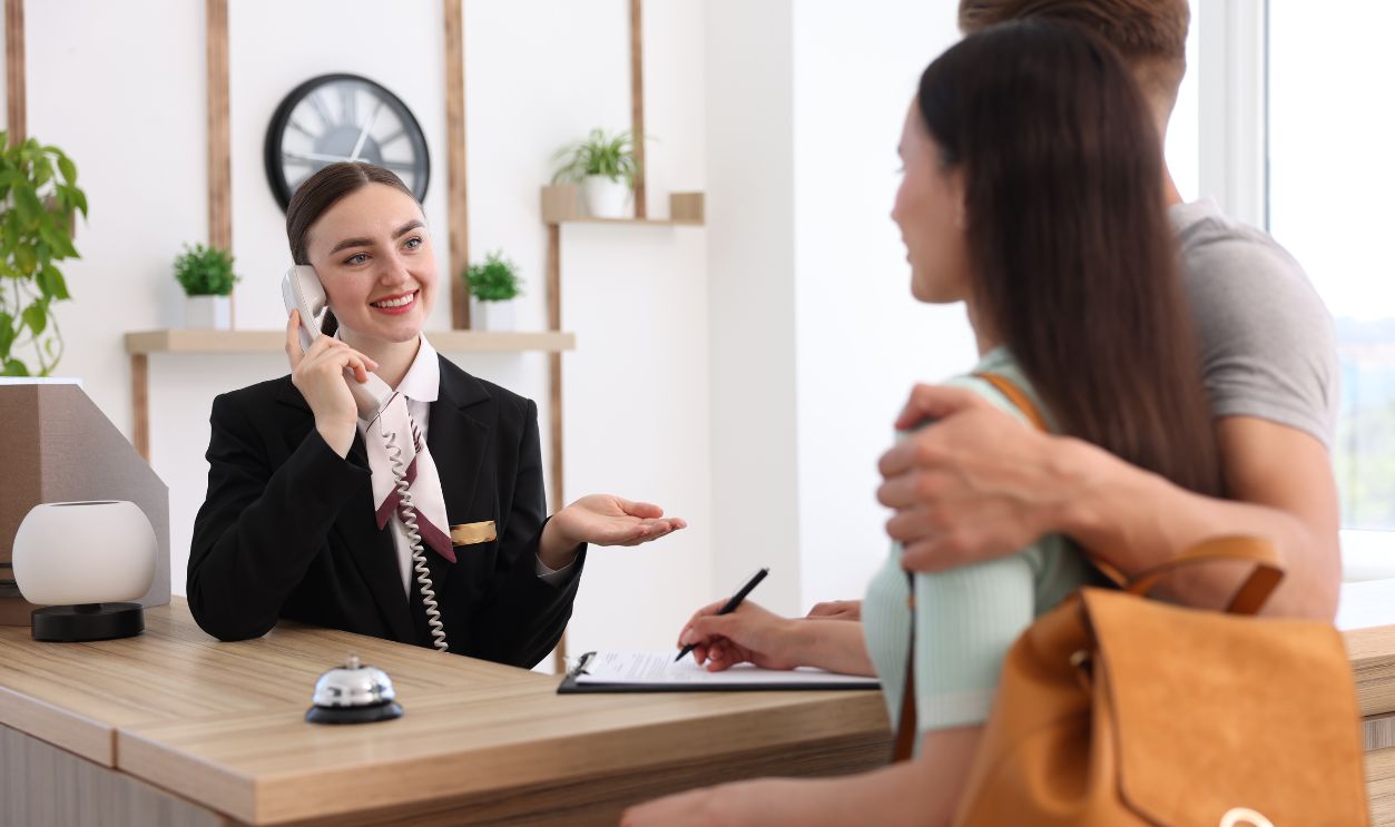  Smiling receptionist working with clients at reception desk in hotel