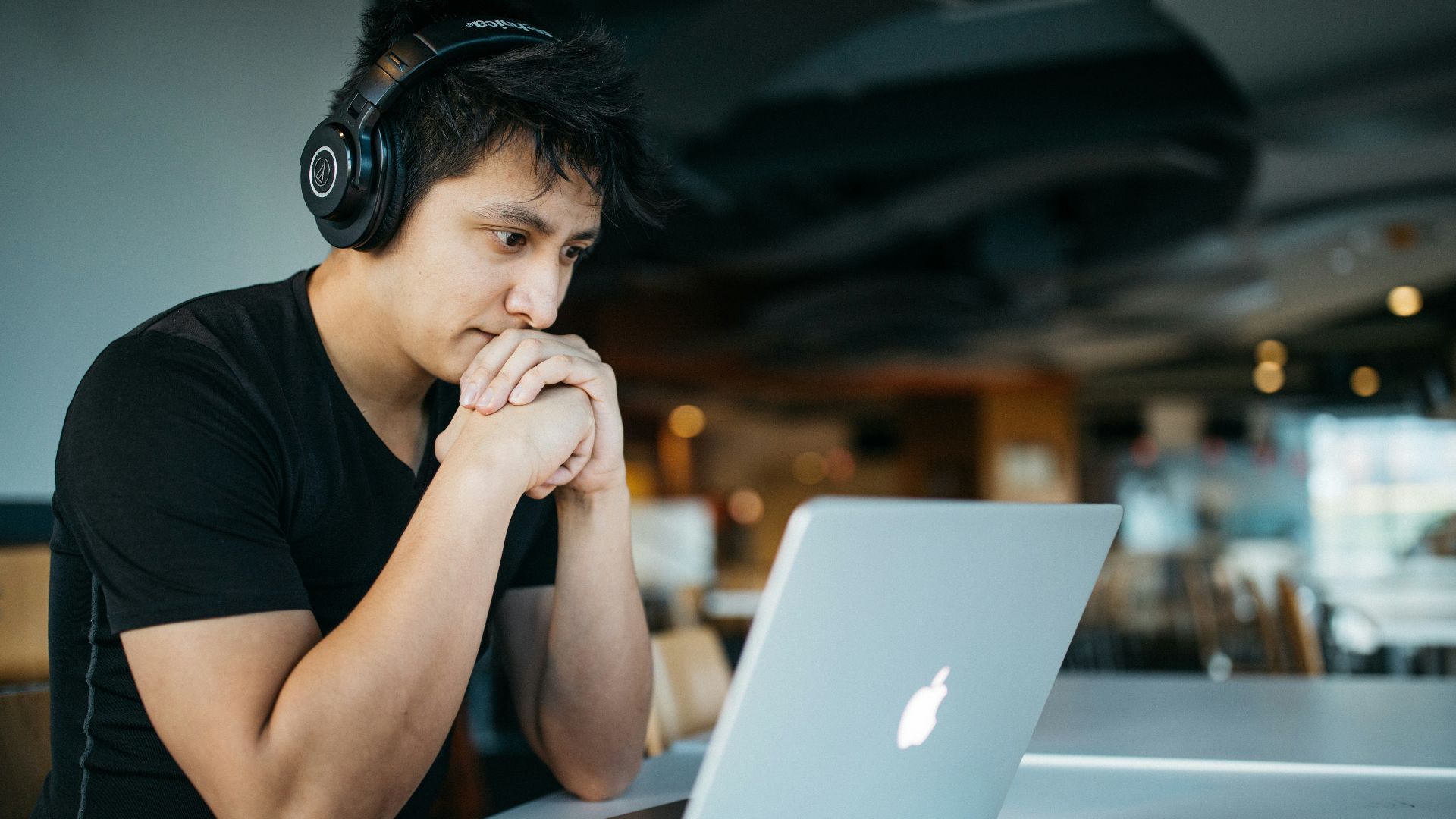 man wearing headphones while sitting on chair in front of MacBook