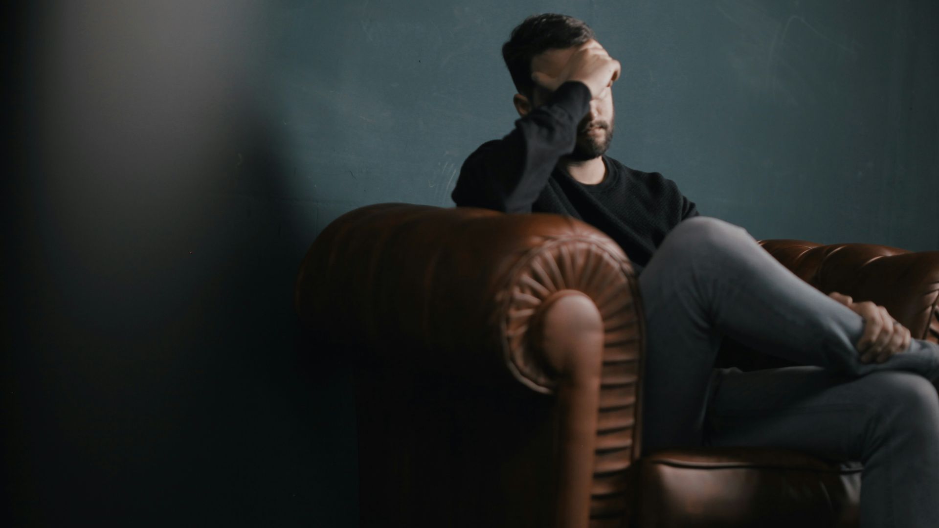 a man holds his head while sitting on a sofa