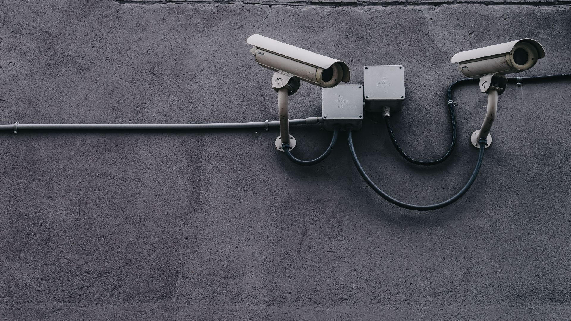 Two surveillance cameras mounted on a concrete wall, highlighting security technology.