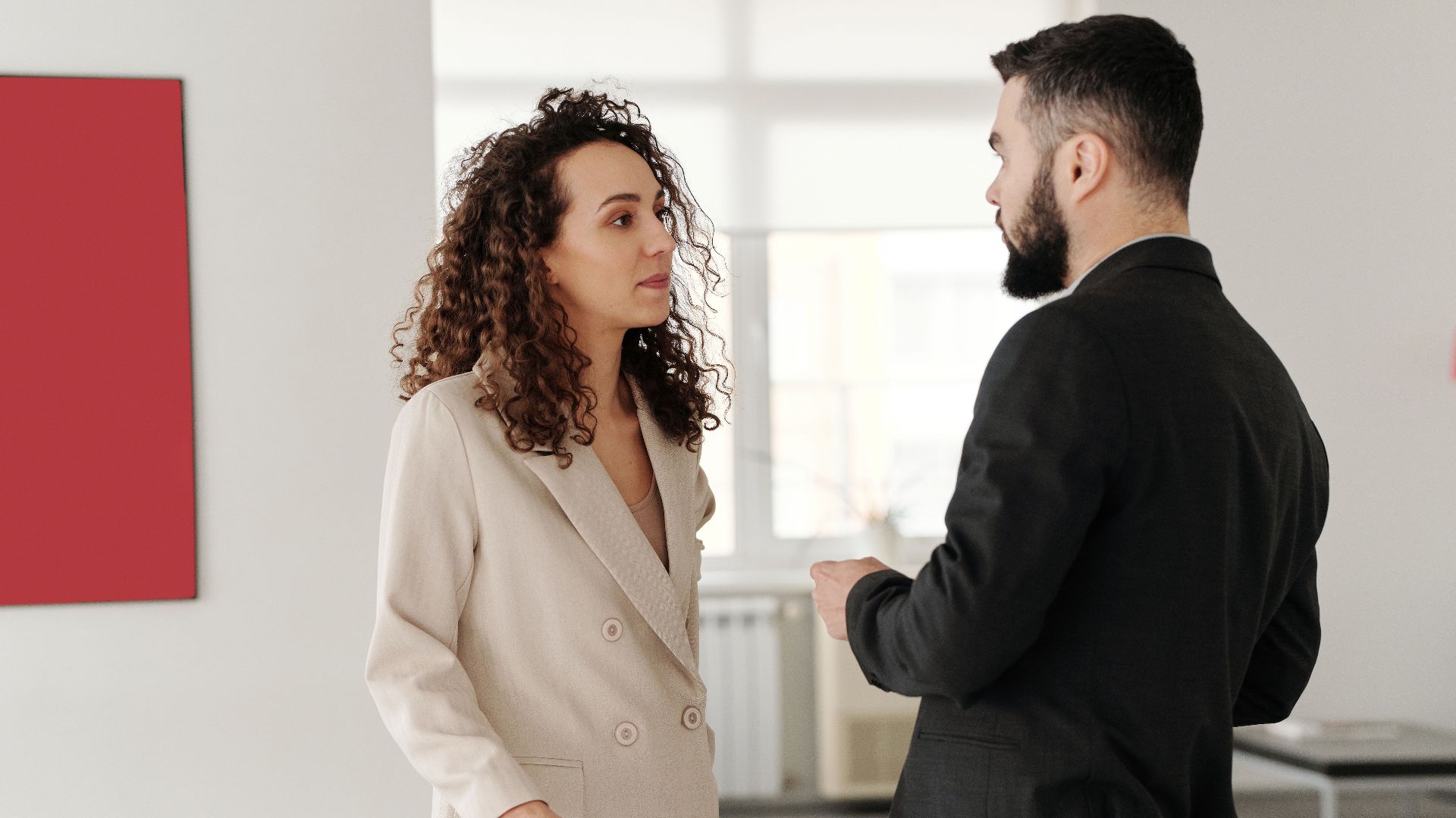 Two professionals engaged in a discussion in a bright, modern office setting.