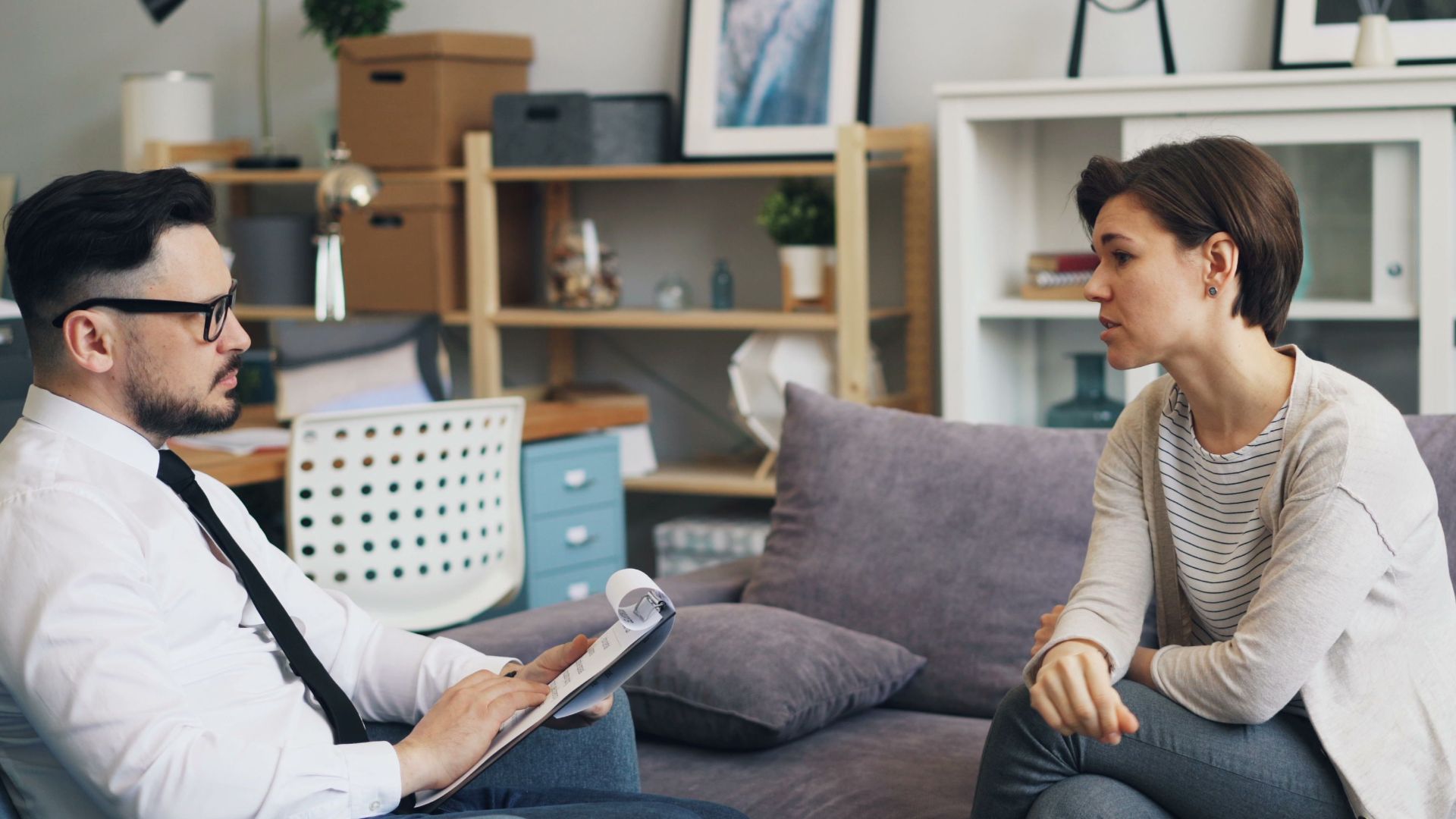 A therapist consults with a client during a counseling session on a sofa in an office setting.
