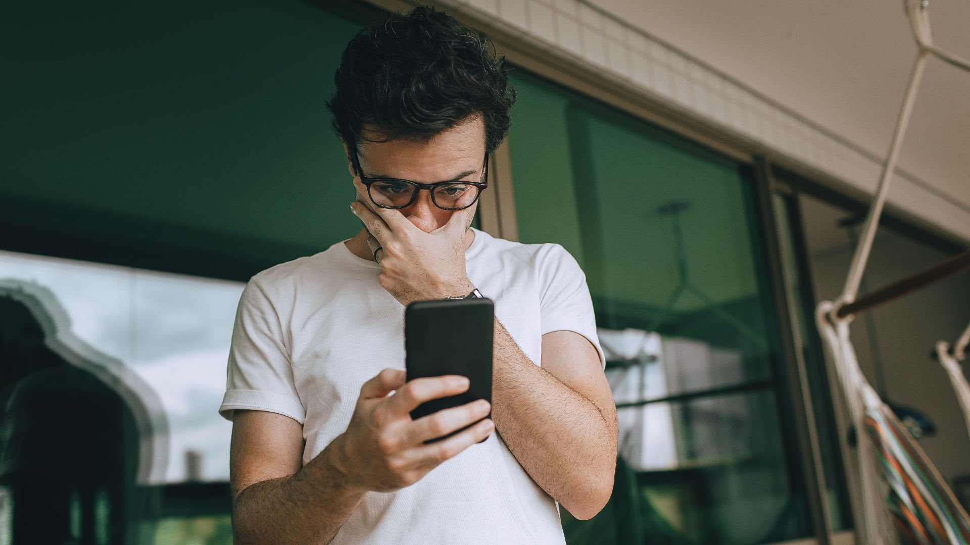 Man with eyeglasses focused on smartphone indoors, captured in a contemplative moment.