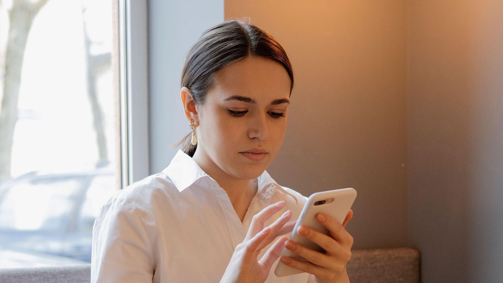 Woman in white shirt using smartphone at a cafe with coffee on the table.