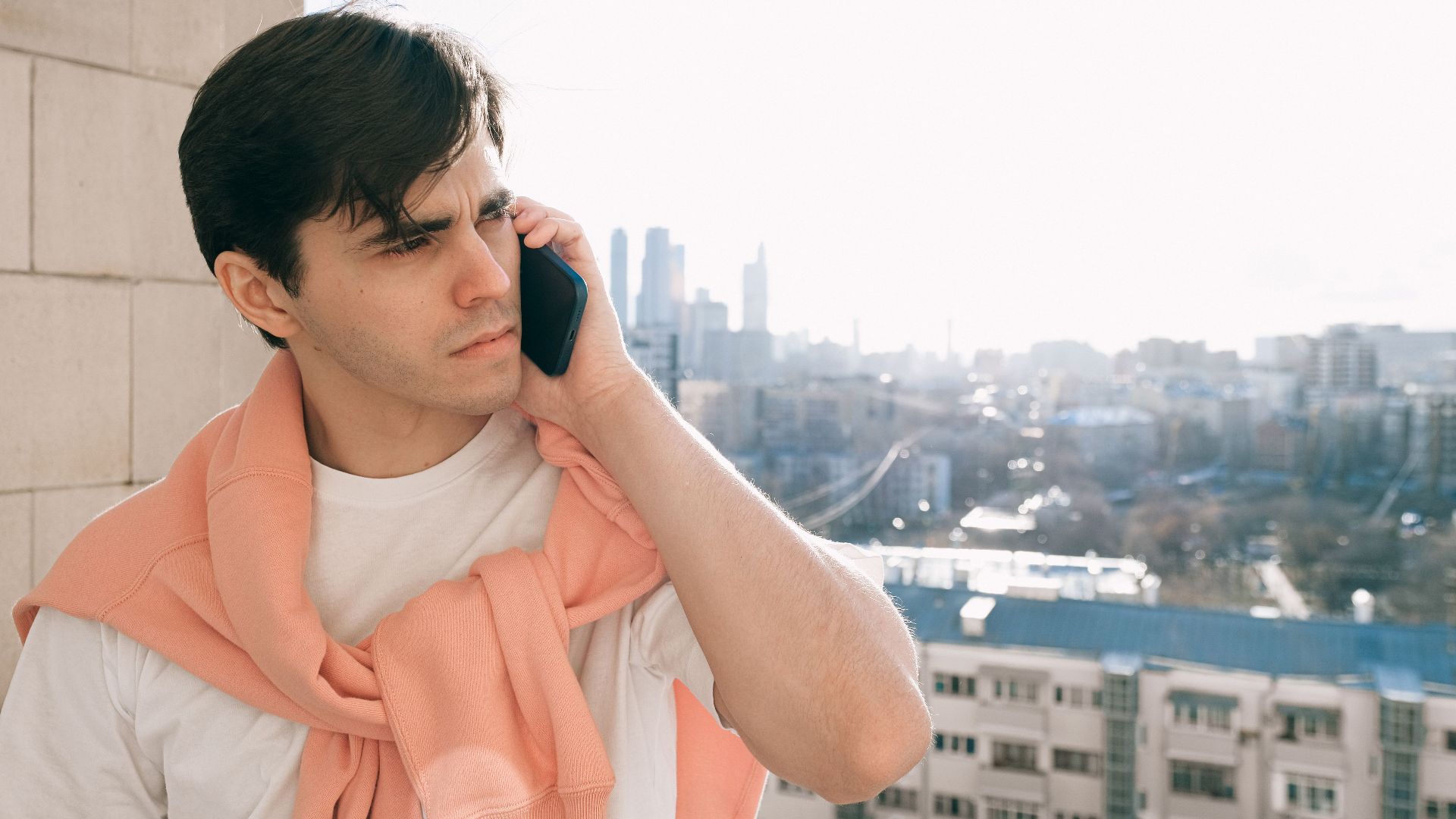 Young adult casually talking on the phone while enjoying a city view from a balcony.
