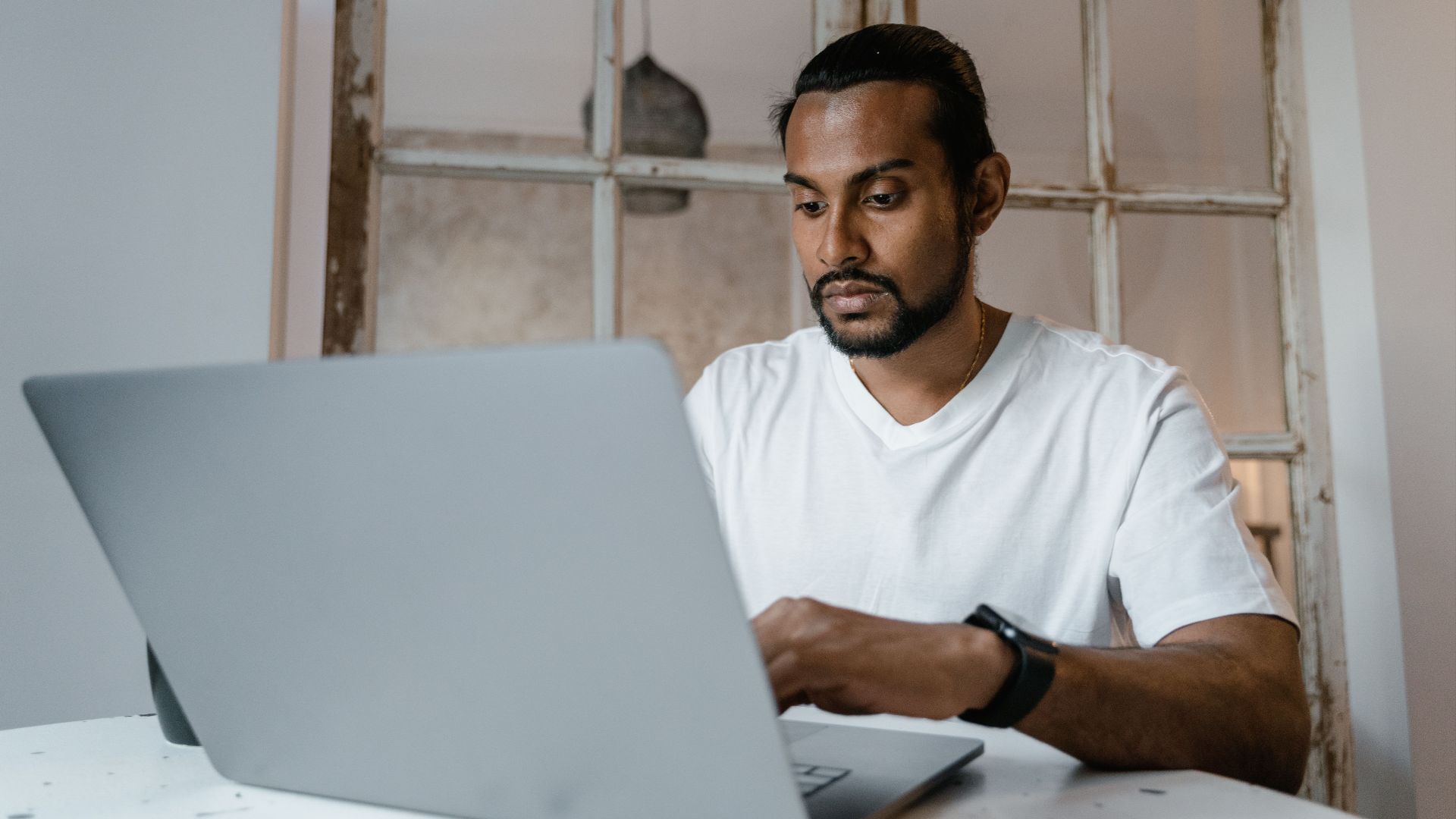 A focused man working on a laptop indoors, emphasizing productivity and concentration.