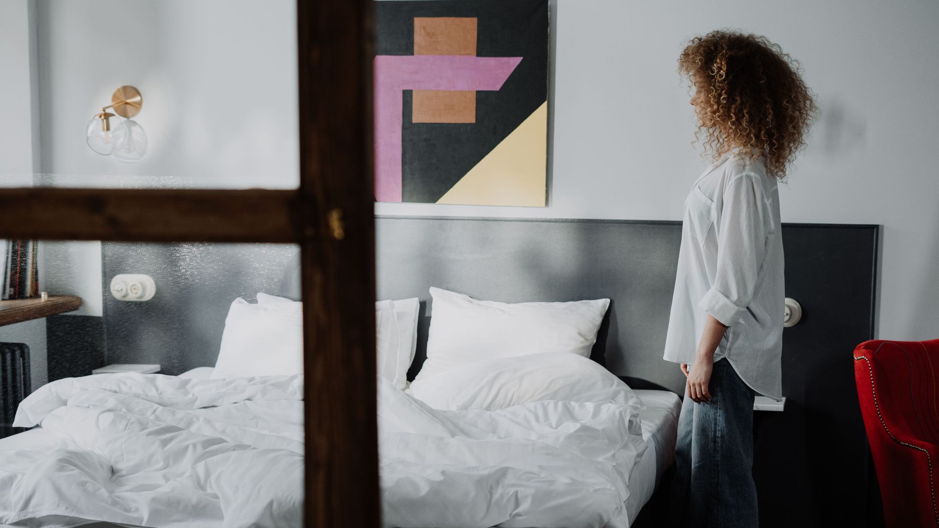 A woman standing in a cozy bedroom with modern art, showcasing a comfortable and stylish interior.