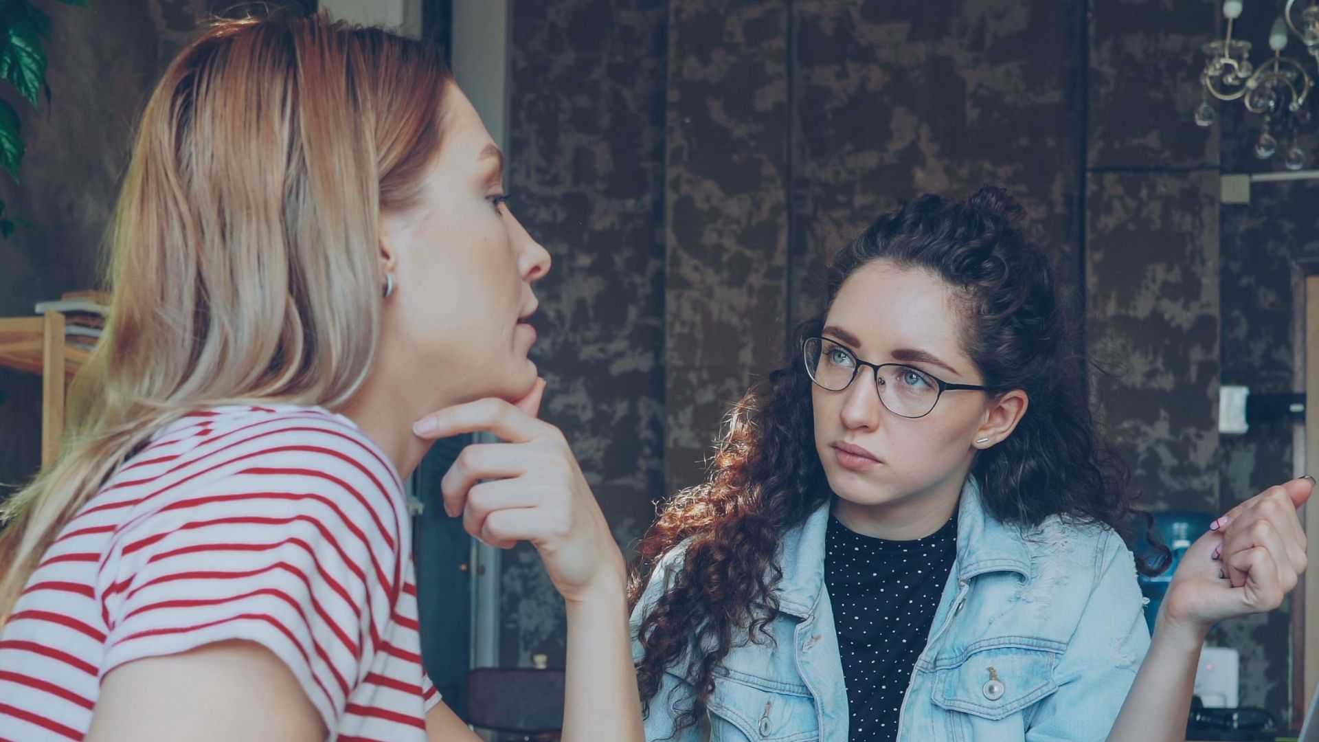 Two women having a serious discussion at a desk with a laptop in a stylish office setting.