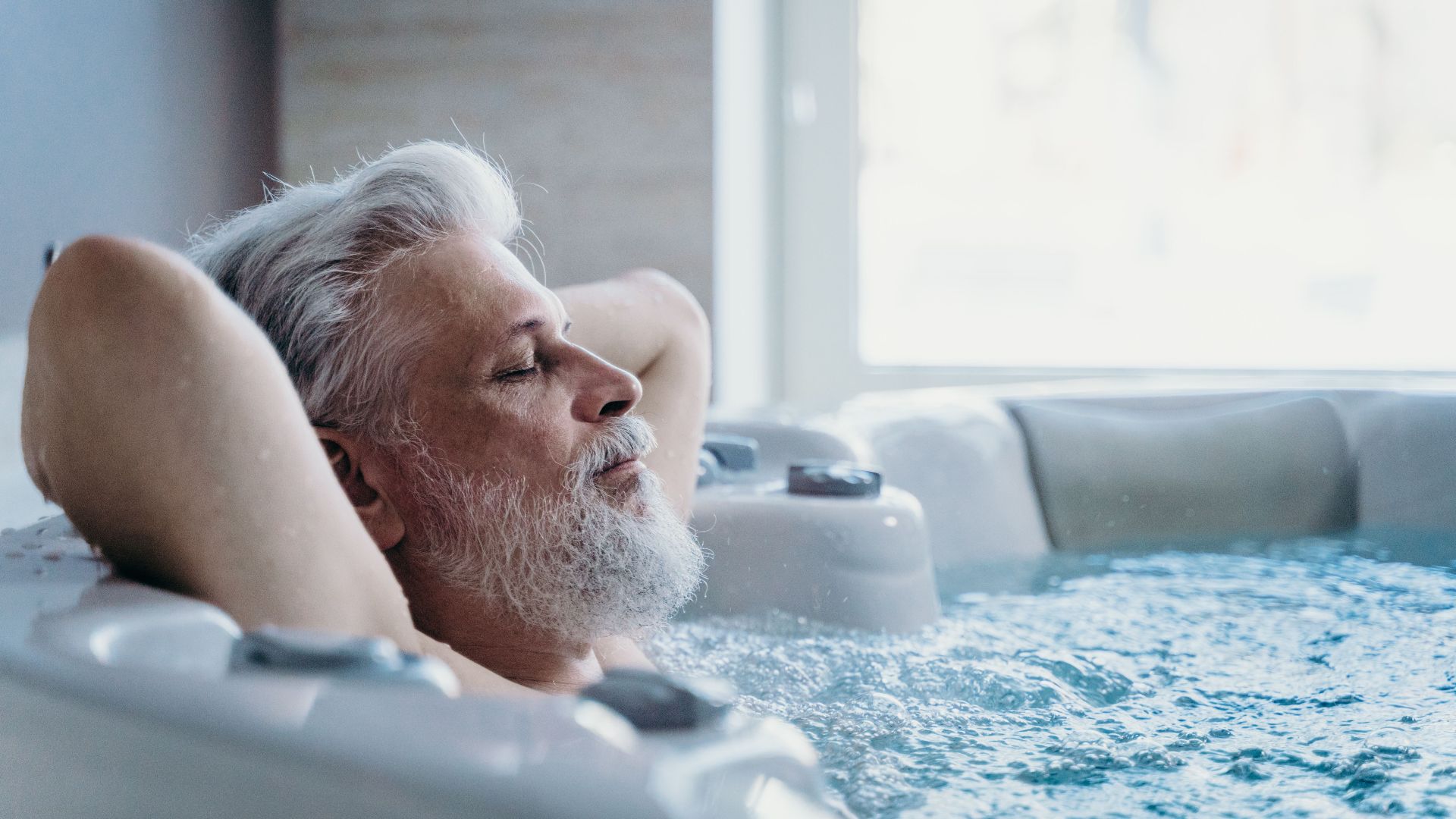 Elderly man with grey hair enjoys relaxation in an indoor jacuzzi, symbolizing wellness and leisure.
