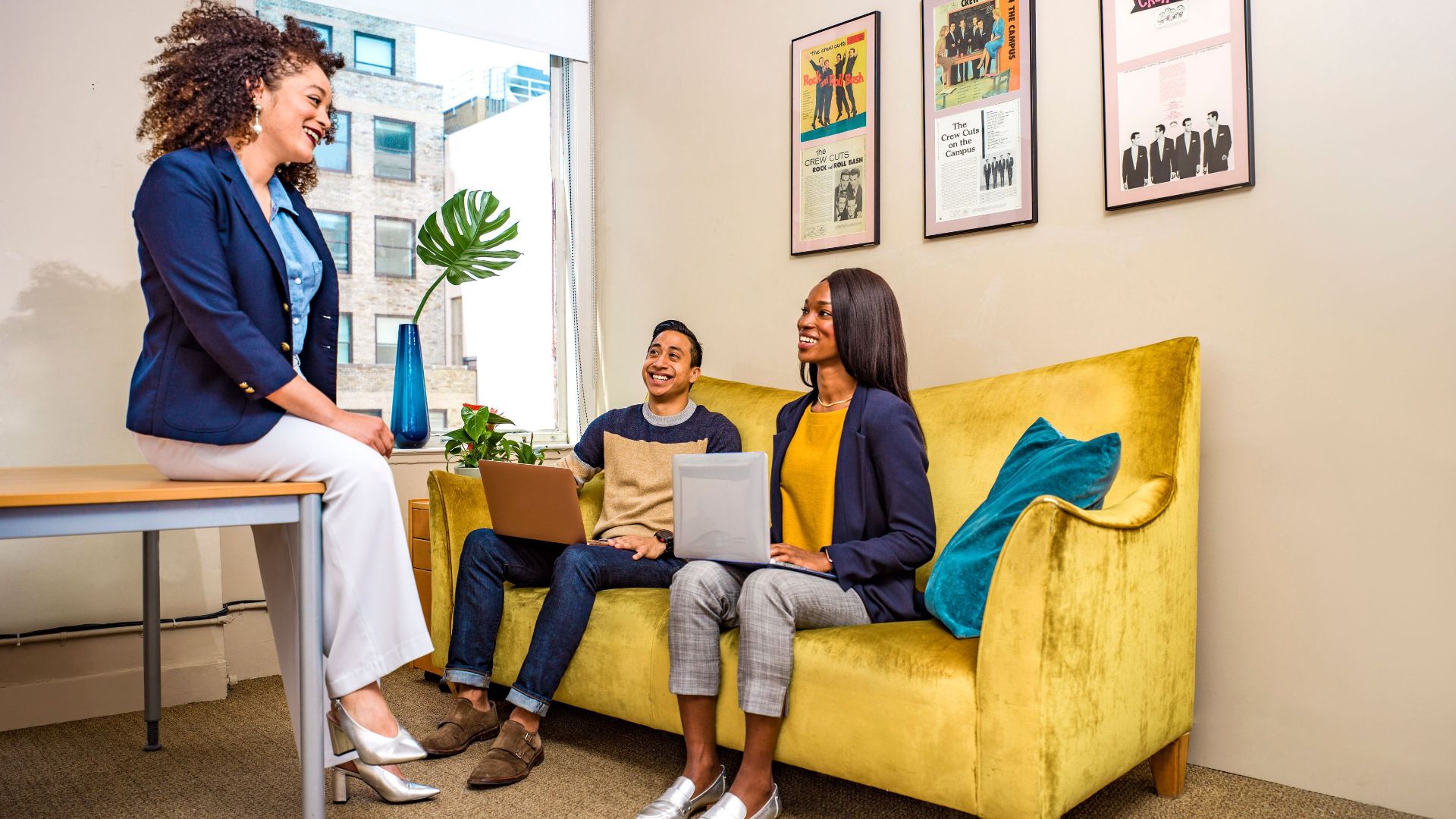 Three professionals engage in a casual meeting in a modern office setting.