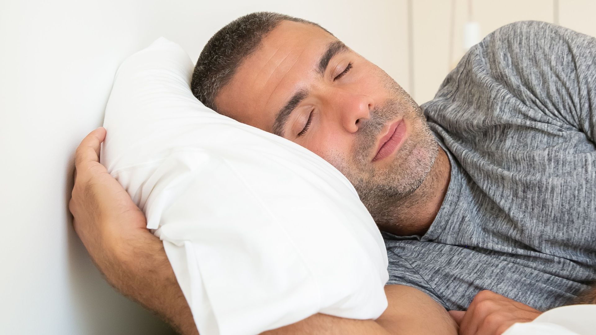 Man with tattoos resting peacefully in bed, eyes closed, embracing a serene sleep.