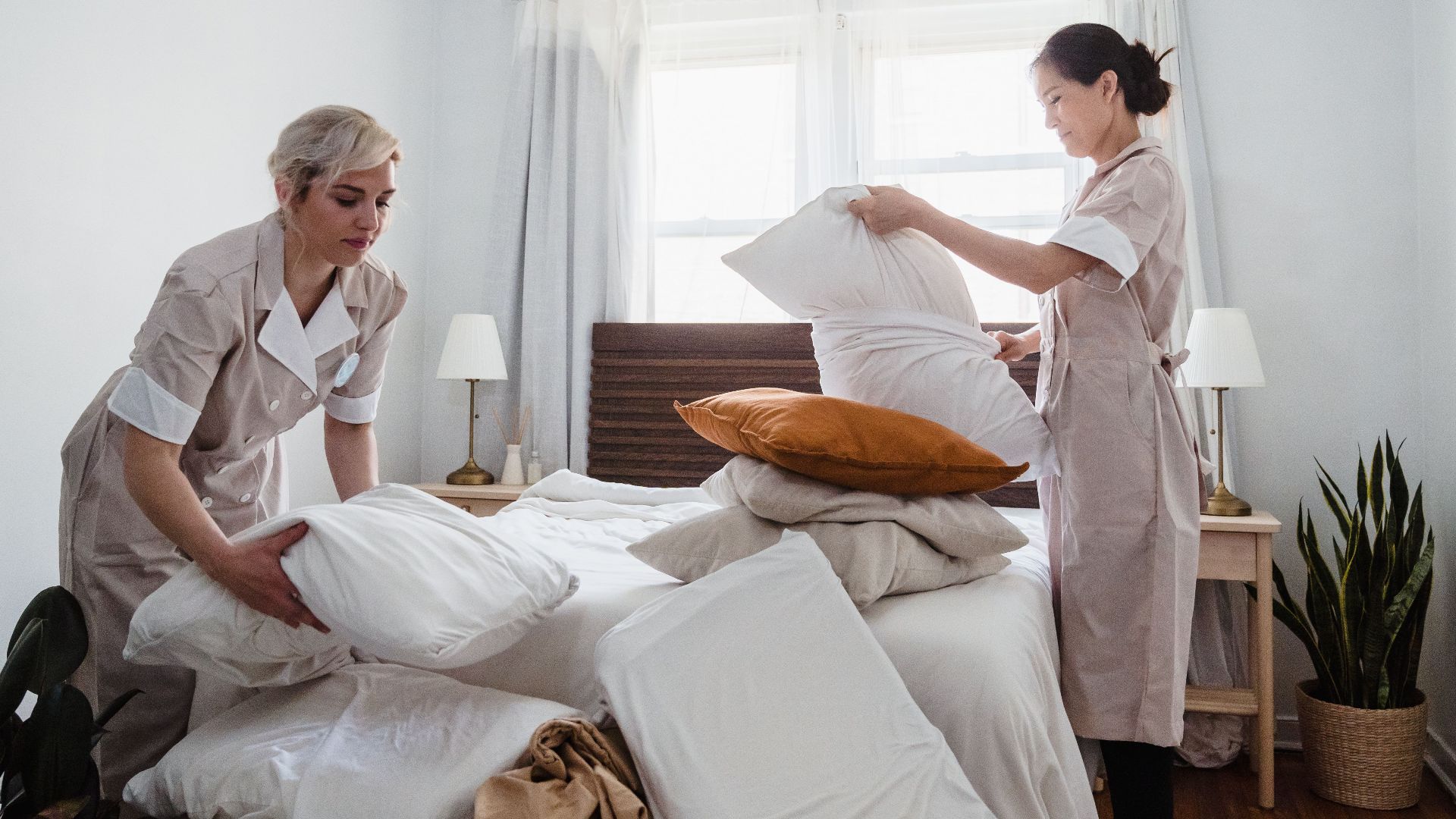 Housekeepers tidying the bed with pillows in a hotel room displaying a clean and organized environment.