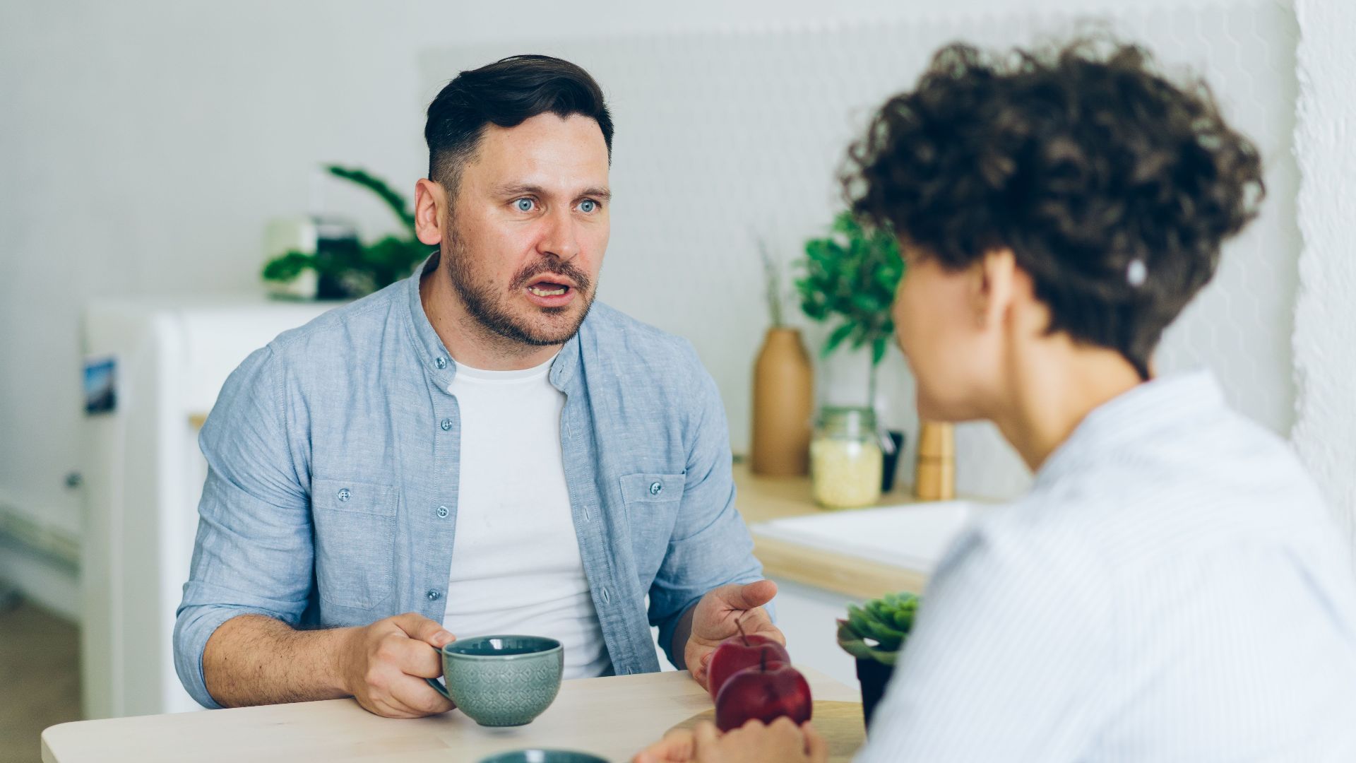 Couple having a serious conversation at the kitchen table with coffee cups.