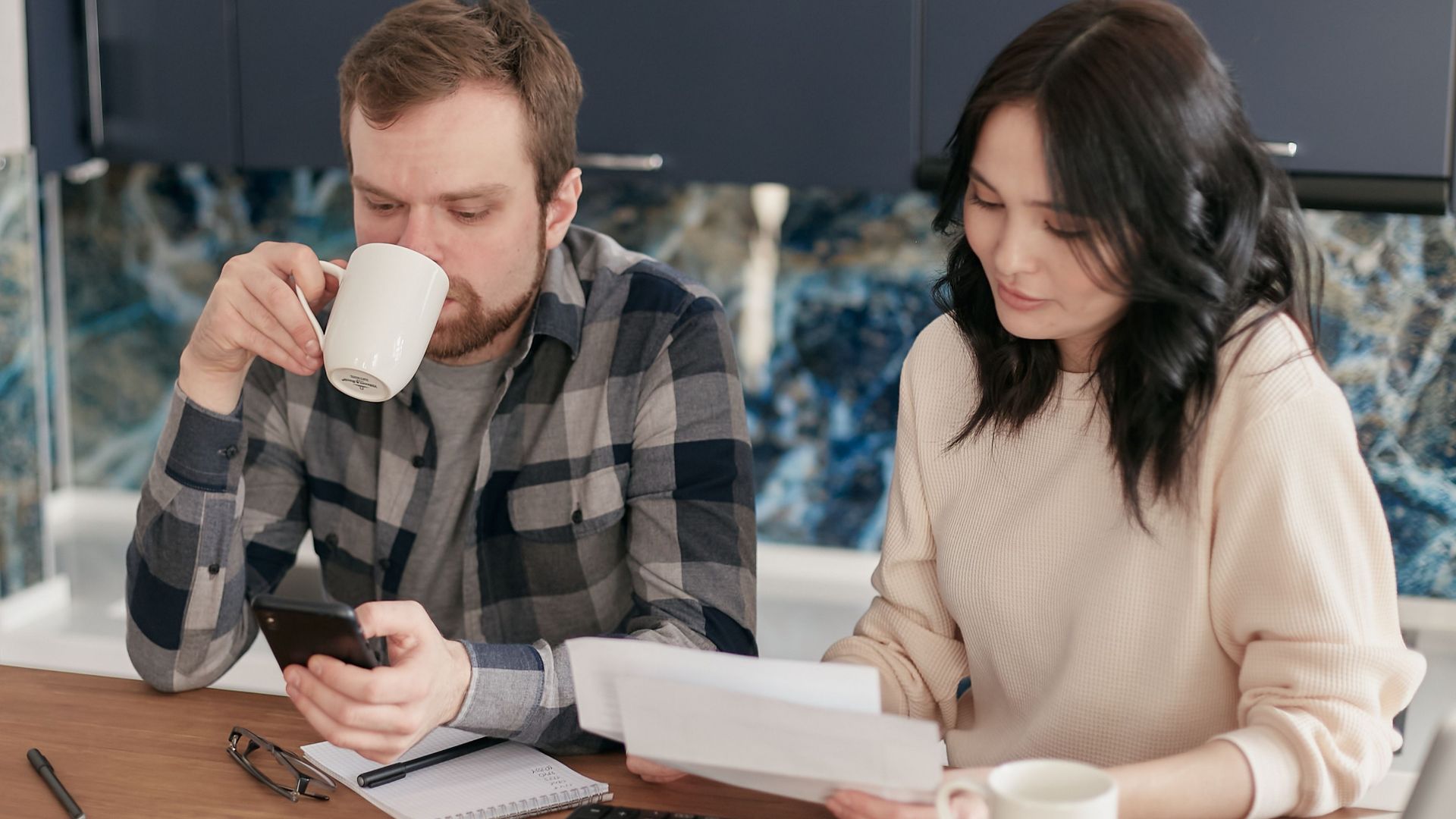 A couple reviewing bills, using a calculator and smartphone, in a modern kitchen.