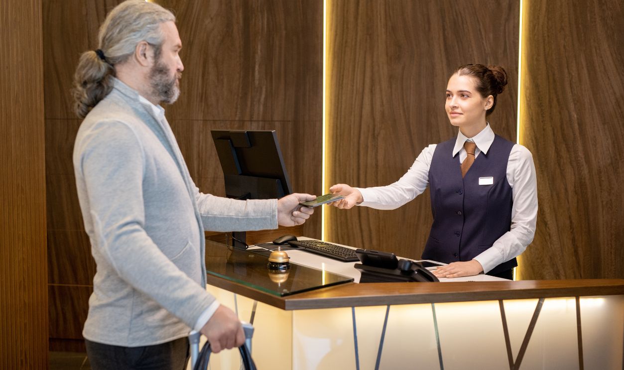 Young receptionist taking documents of mature man over counter