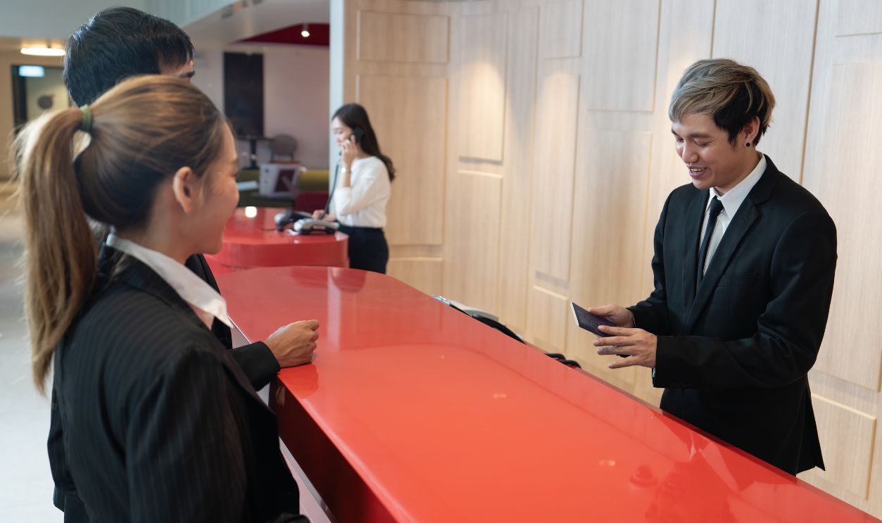 Shutterstock-2192687347, In the hotel lobby guest reception counter front desk staff greeting and talking while checking passport during check in and issue key card and breakast coupon before calling bell boy