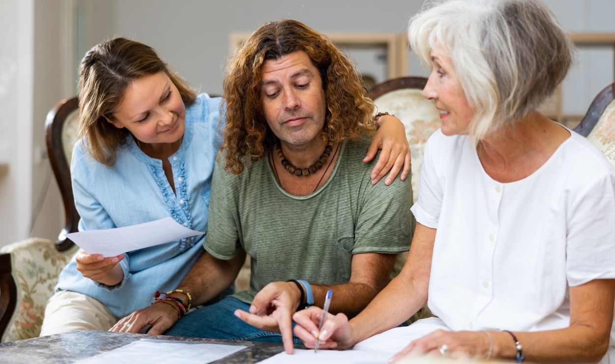 Shutterstock-2240577273, Mature woman at table in home room filling up documents with family