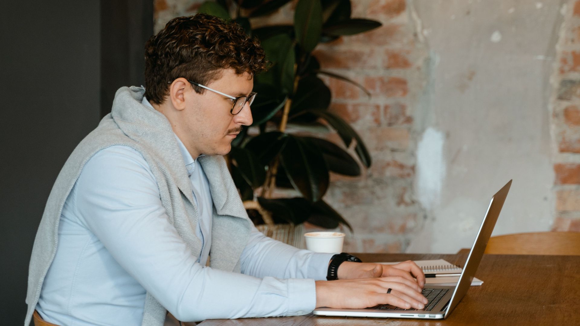 Man typing on laptop at a wooden desk in a cozy, rustic office space.