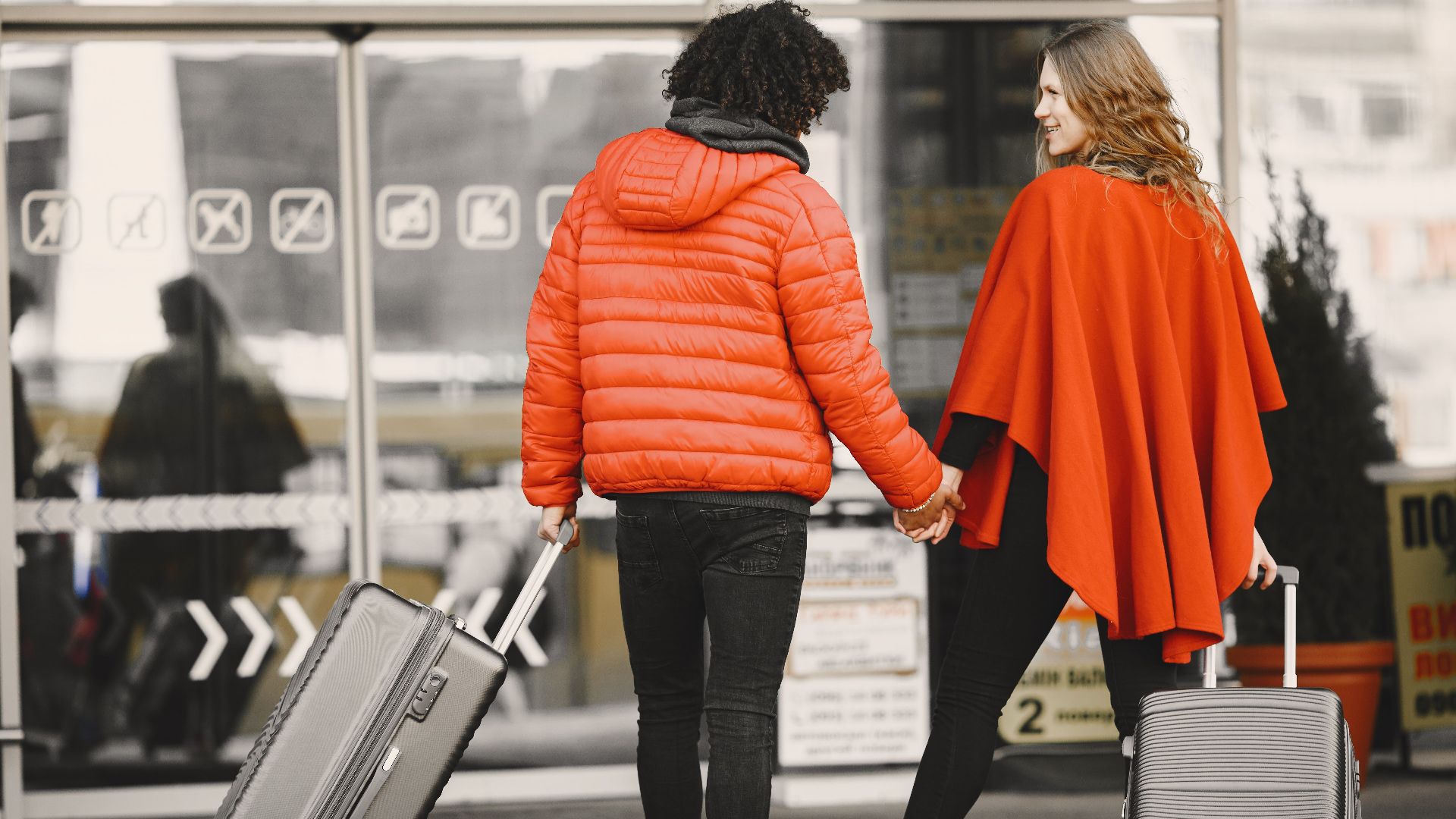 A couple holding hands with luggage, entering an airport for a travel journey.