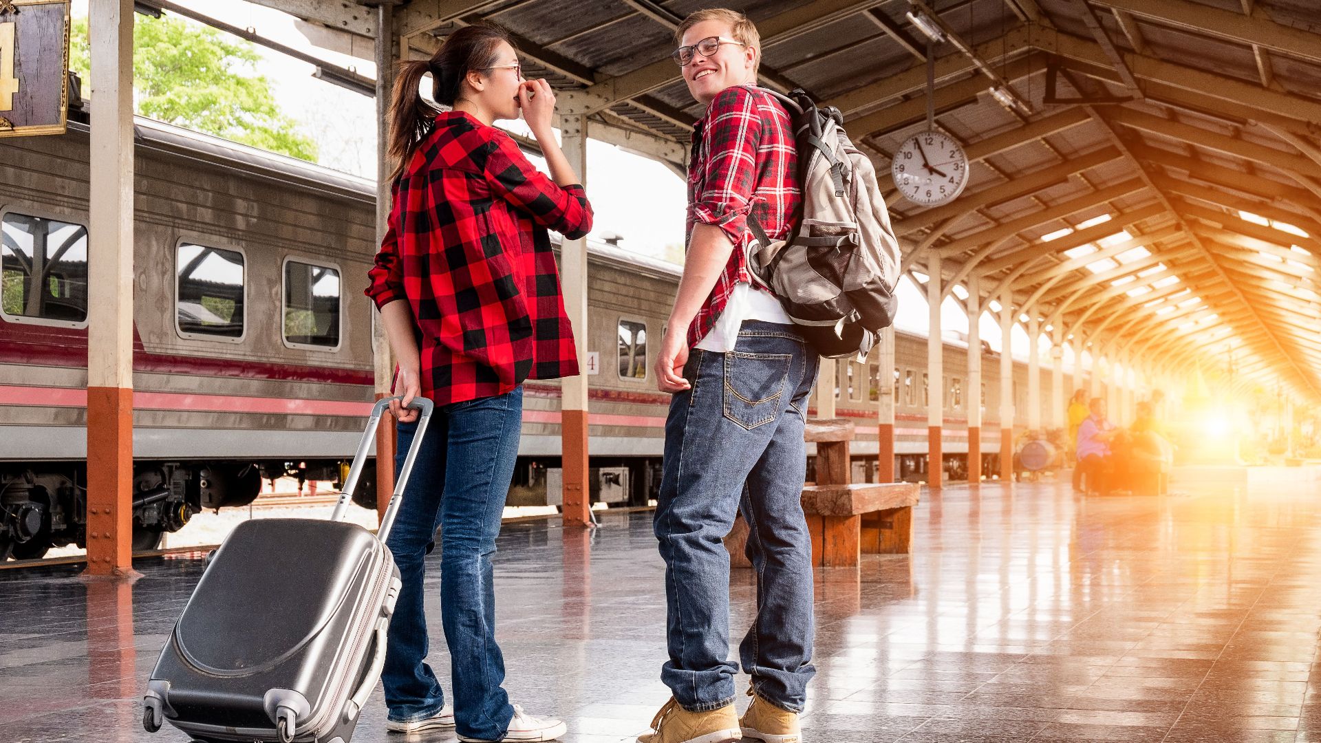 Young couple in a railway station, ready for travel. Bright morning scene with backpacks and luggage.