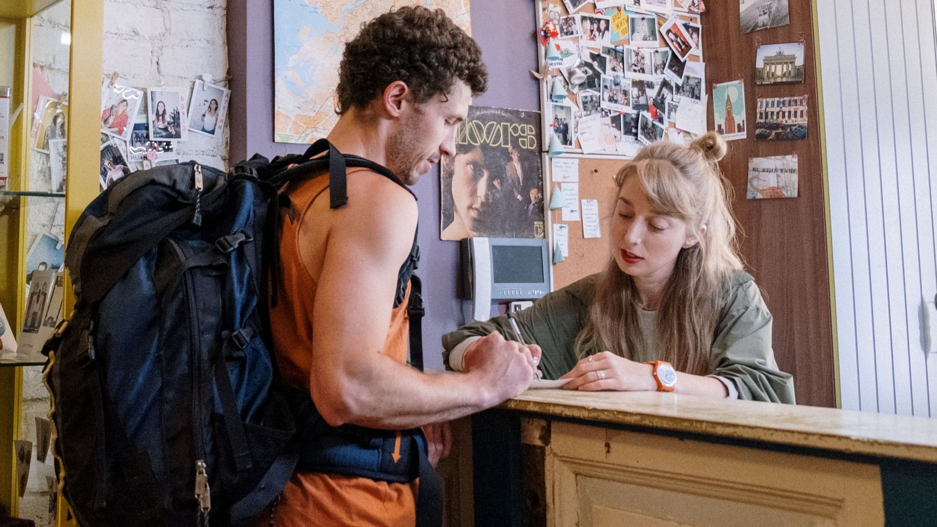 A backpacker at a hostel front desk getting assistance from a receptionist.