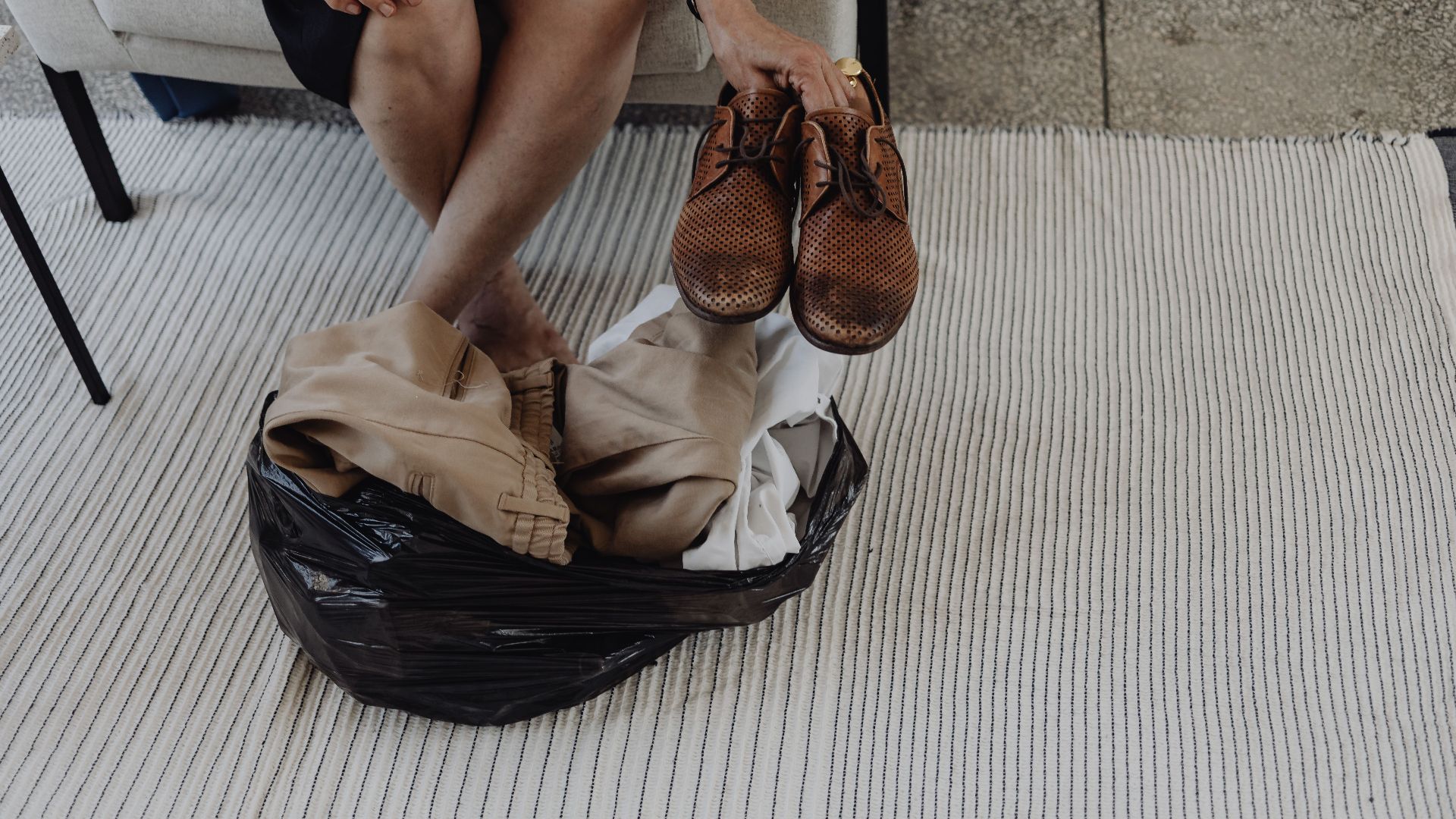 Adult sitting on carpet arranging clothes and shoes from a bag indoors.