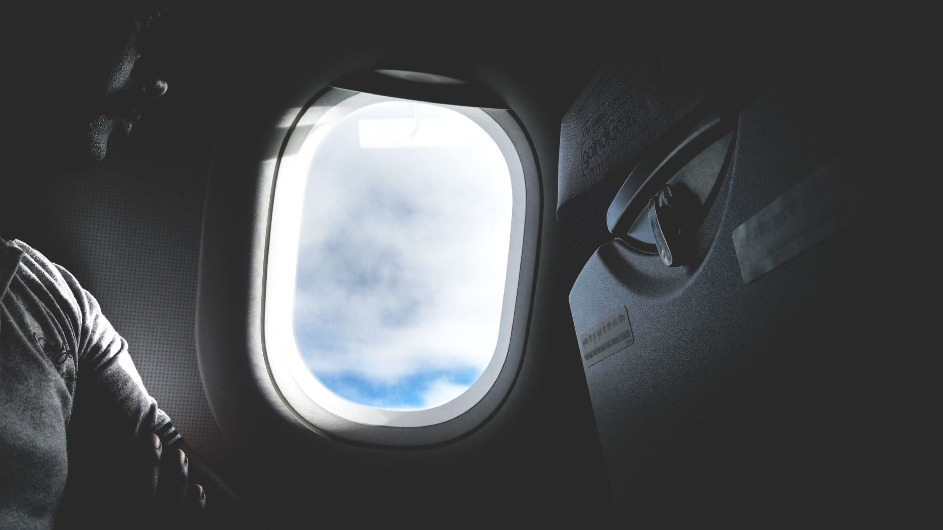 Silhouette of a passenger looking through an airplane window at the clouds outside.