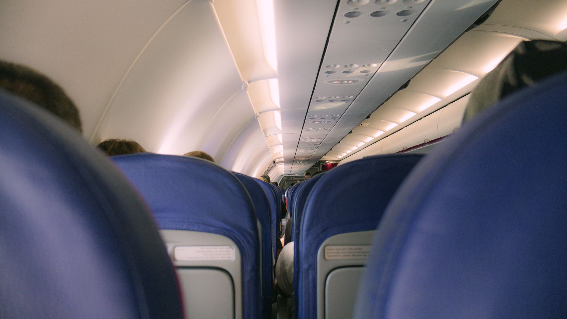 A view of a modern airplane cabin showing rows of blue seats and overhead compartments.