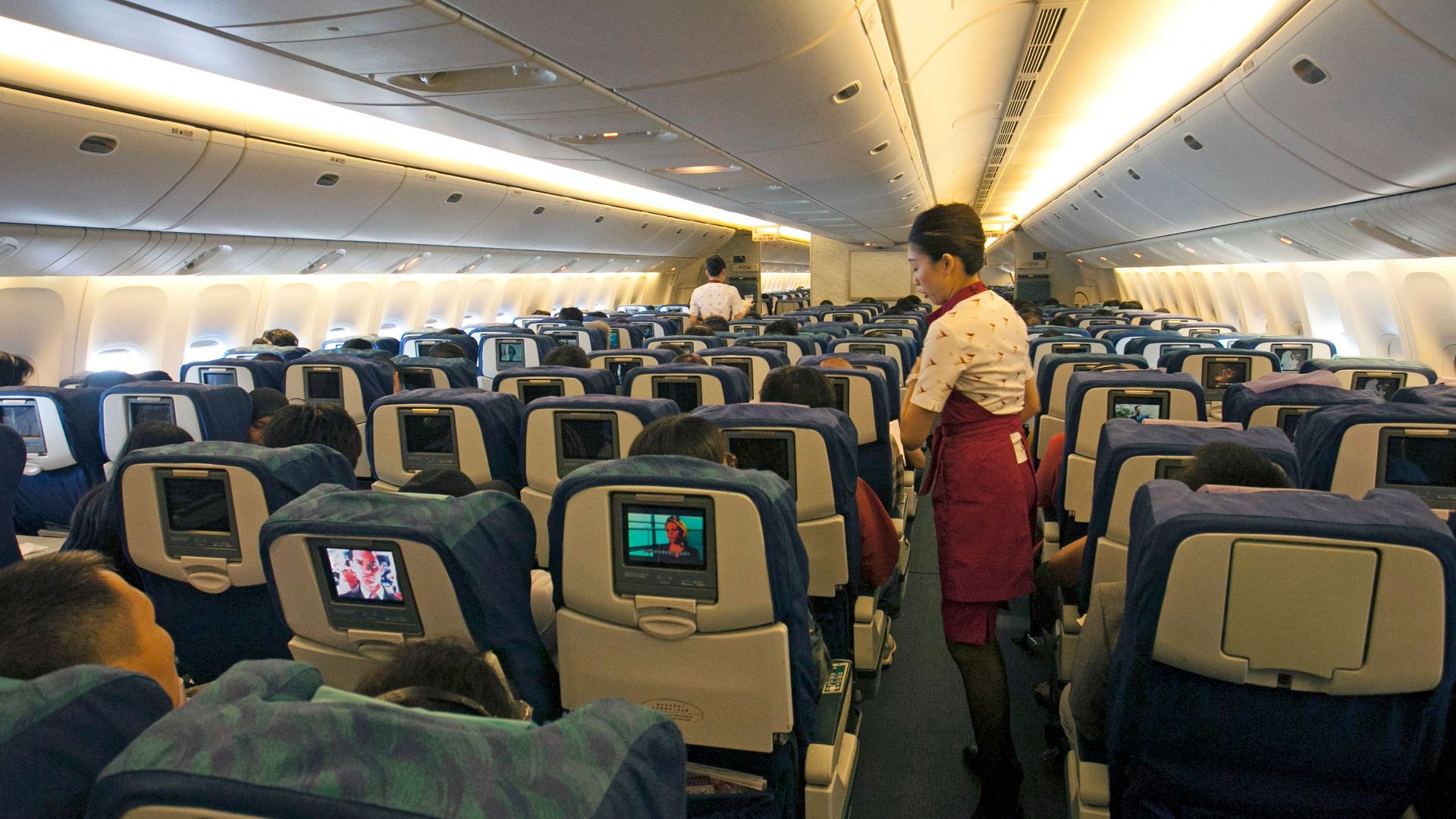 Flight attendant assisting passengers in a busy airplane cabin, ensuring a comfortable travel experience.