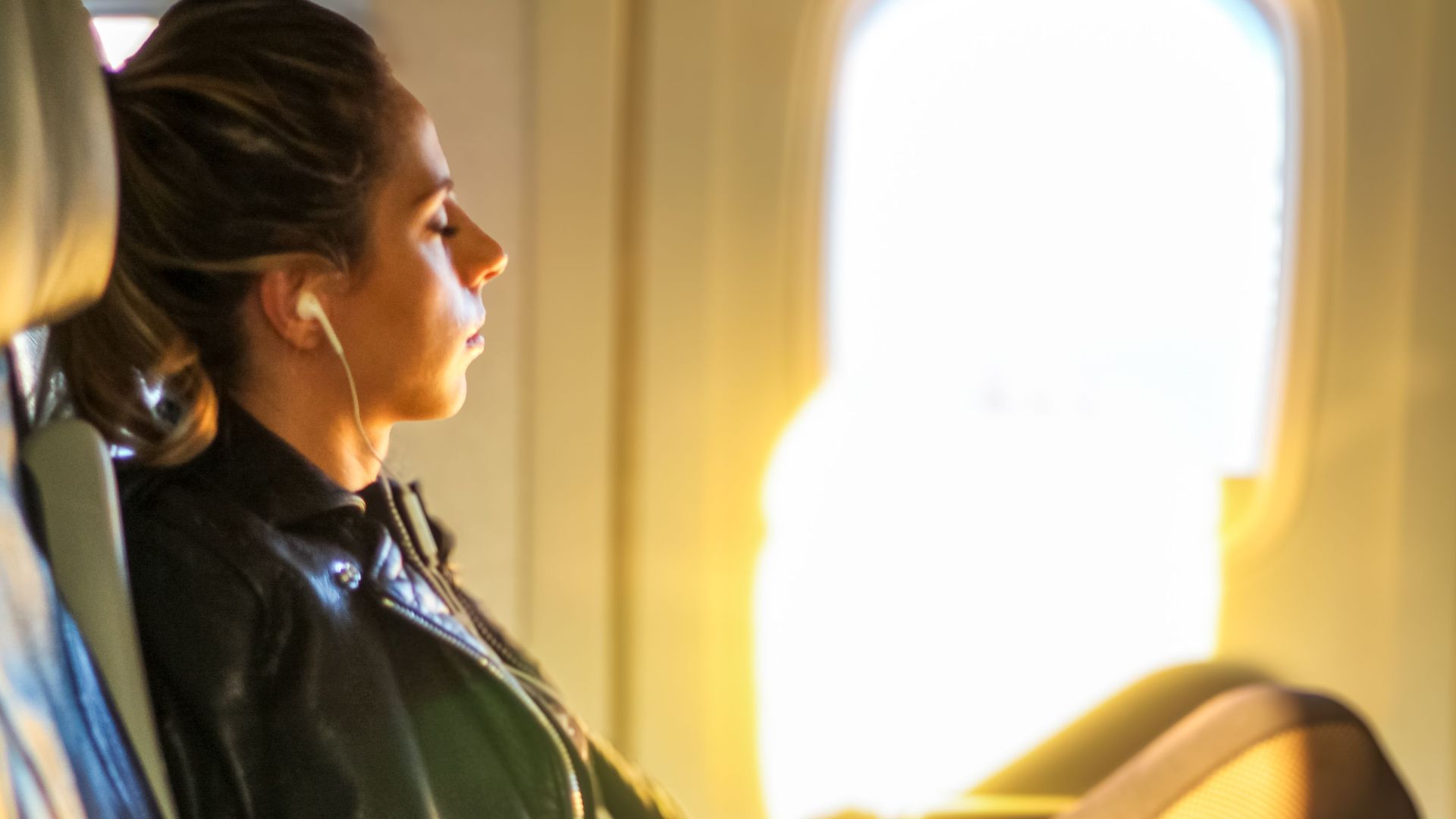 A woman enjoys a tranquil moment on a flight, gazing out the window with headphones on.