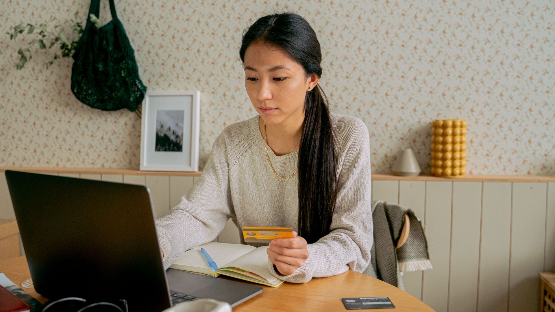 A woman using a laptop and credit card for online shopping at a cozy indoor setting.