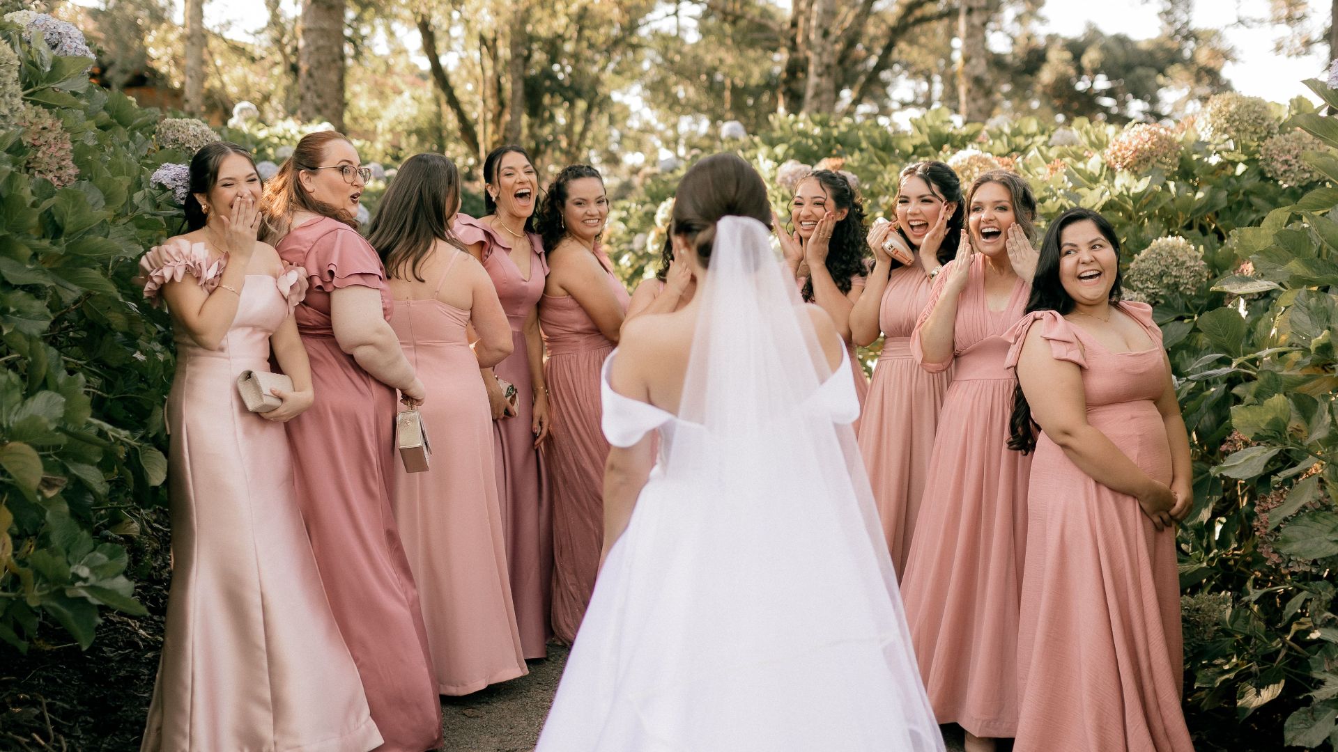 A joyful moment with a bride and bridesmaids in pink dresses outdoors in a forest.