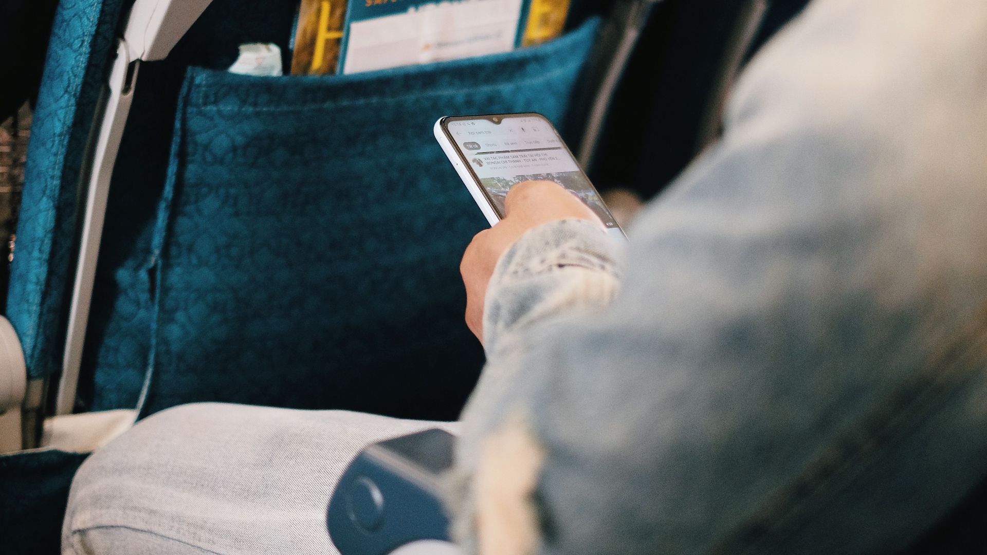 Passenger using smartphone while seated on airplane for entertainment or work.