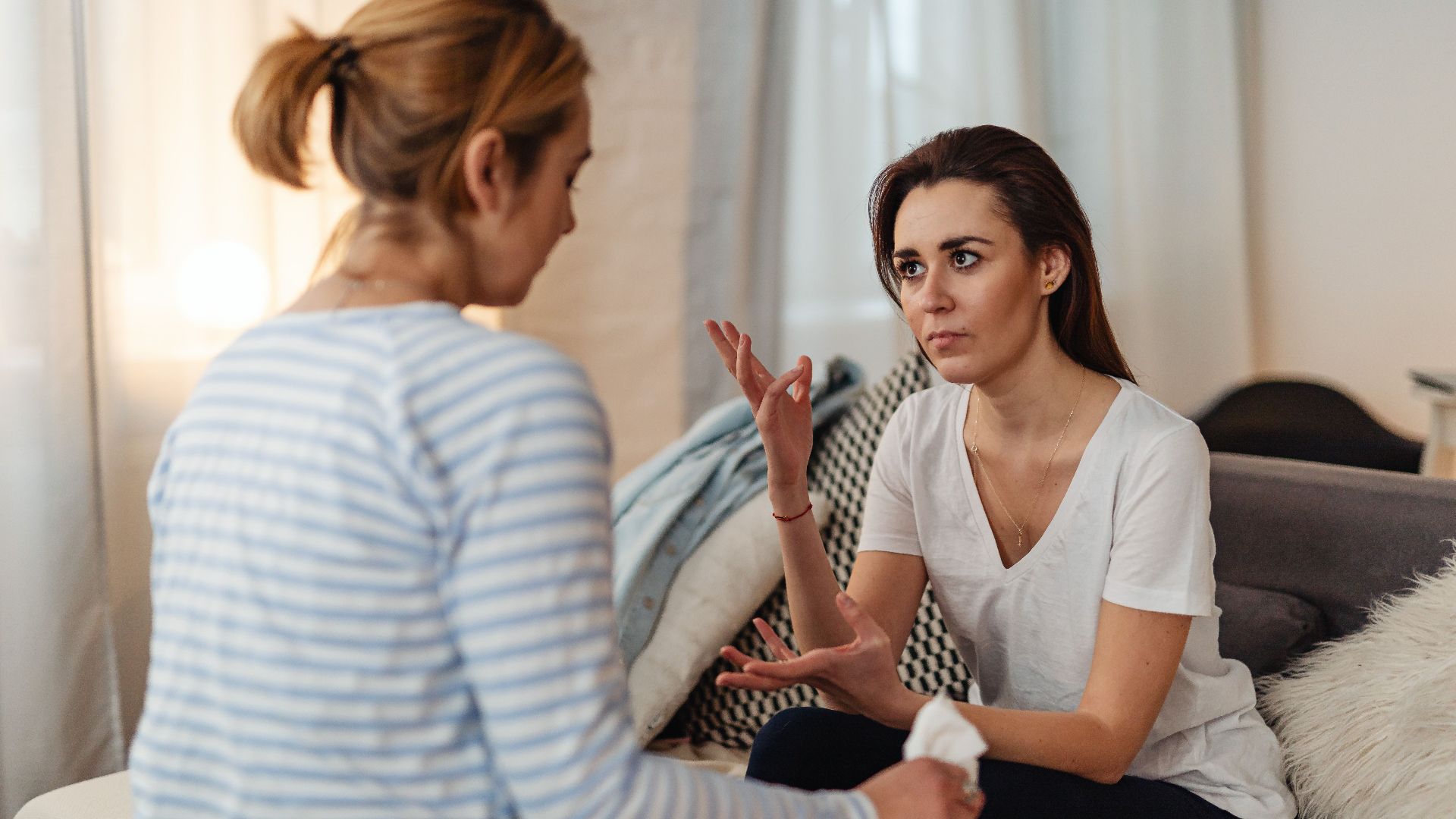 Two women sitting on a sofa, engaged in a serious discussion at home.