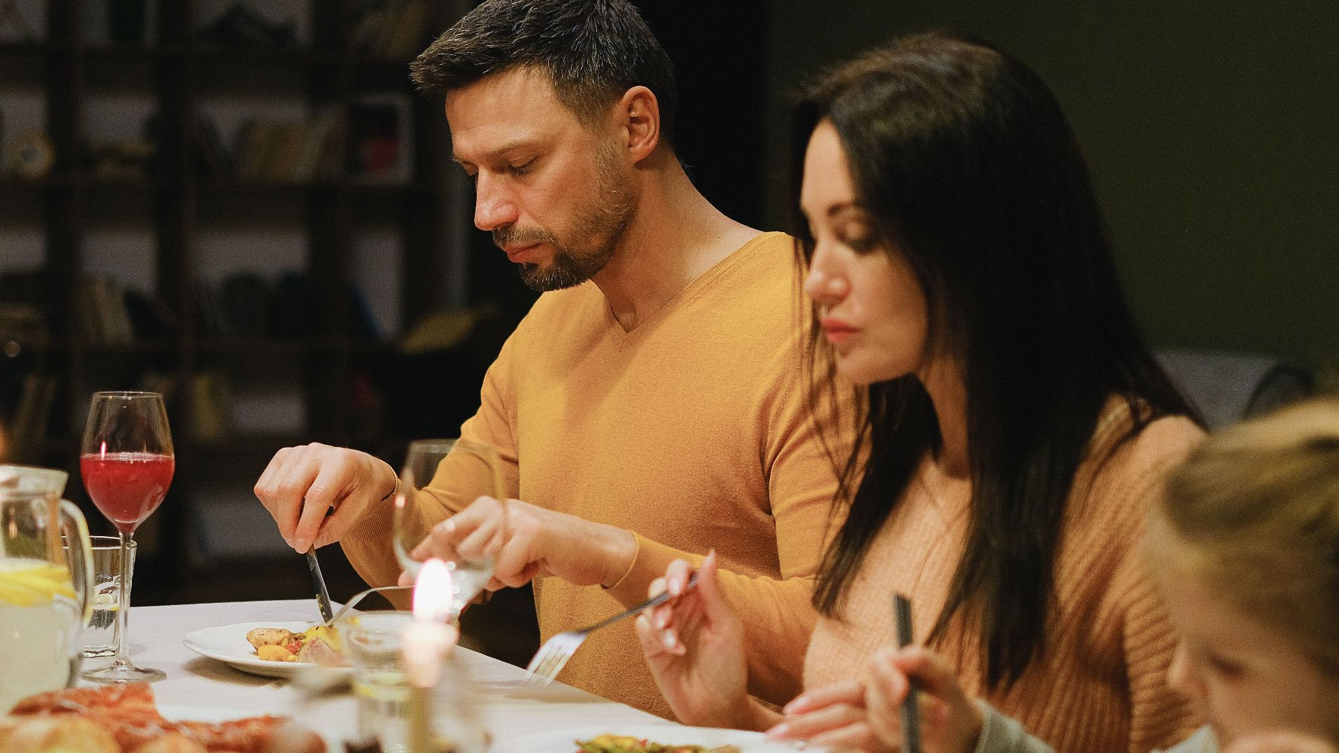 A family gathered around a dinner table indoors, enjoying a meal together with wine and candles.