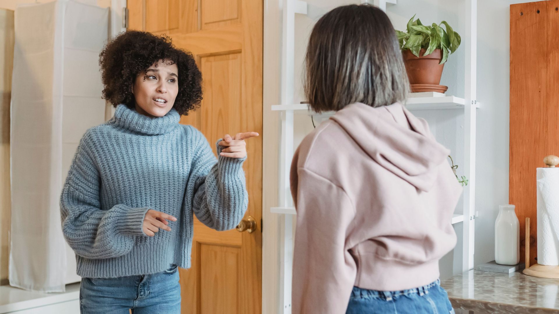 Angry African American female complaining and pointing at faceless female while having fight i modern flat with green plants
