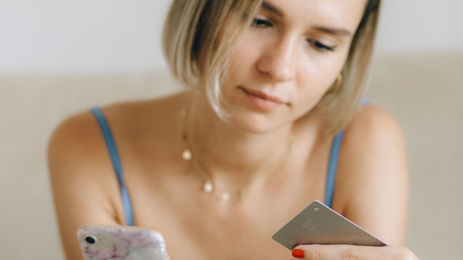 Young woman sitting indoors using her smartphone and a credit card for online shopping.