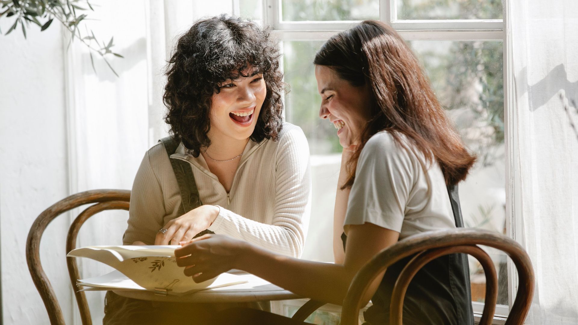 Laughing multiracial female colleagues wearing uniform flipping pages of papers while discussing work together