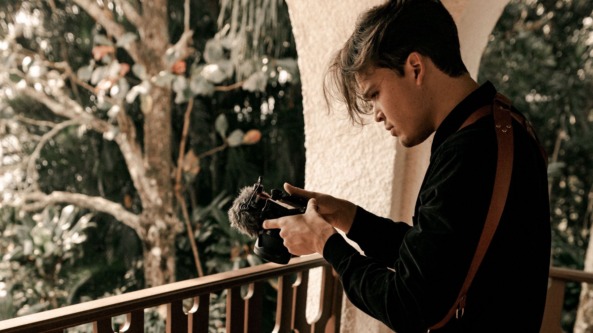 Man on balcony capturing creative shot with camera in natural light.