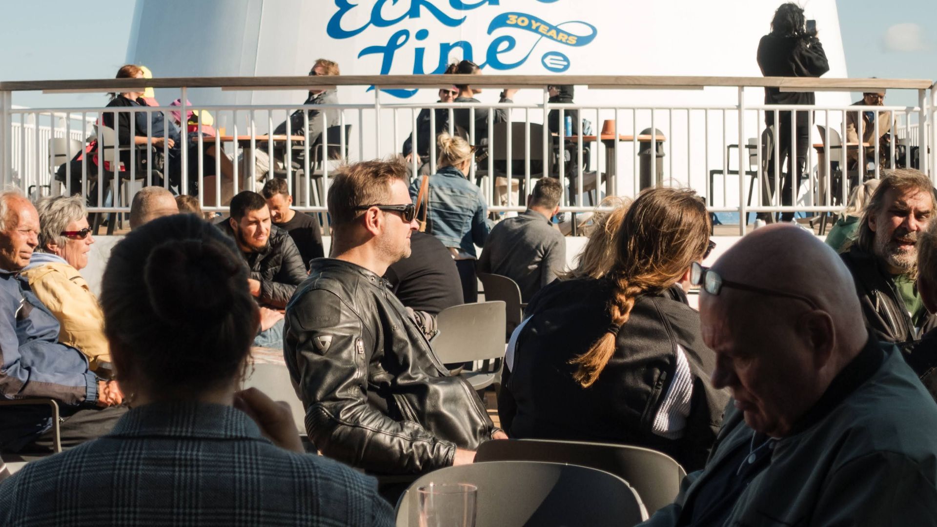 Travelers enjoying the sunny deck on an Eckerö Line ferry under clear skies.