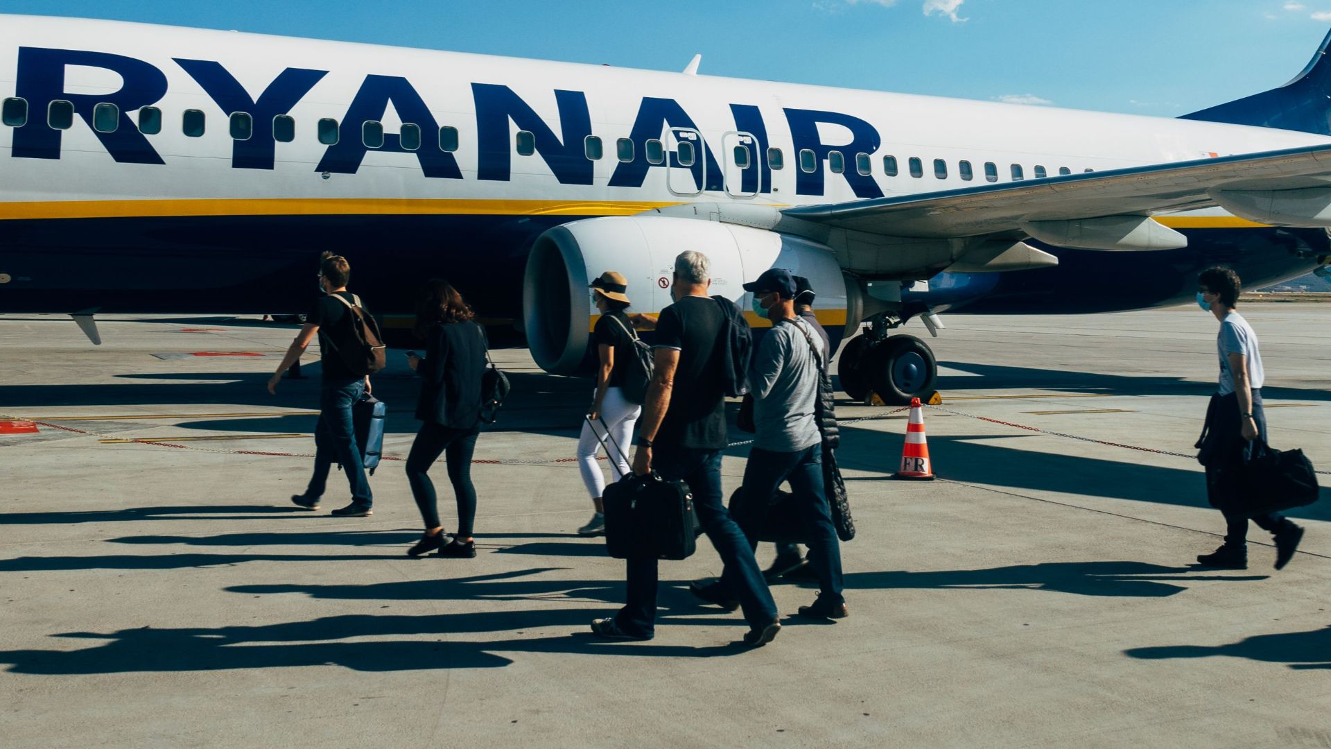 Travelers boarding a Ryanair airplane under clear blue sky at the airport.