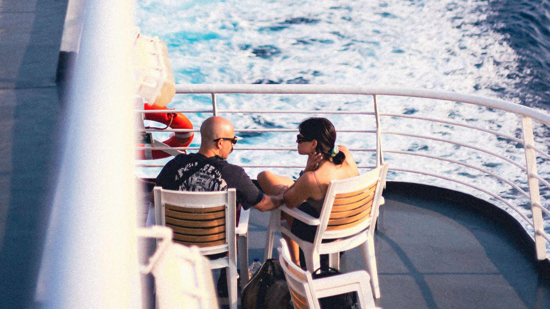 Couple enjoying a calm cruise on a ship, surrounded by ocean waves and clear skies.