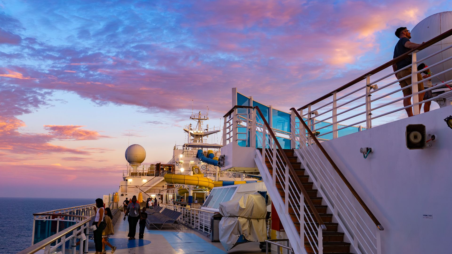 Beautiful view of a cruise ship deck with passengers enjoying a colorful sunset over the ocean.
