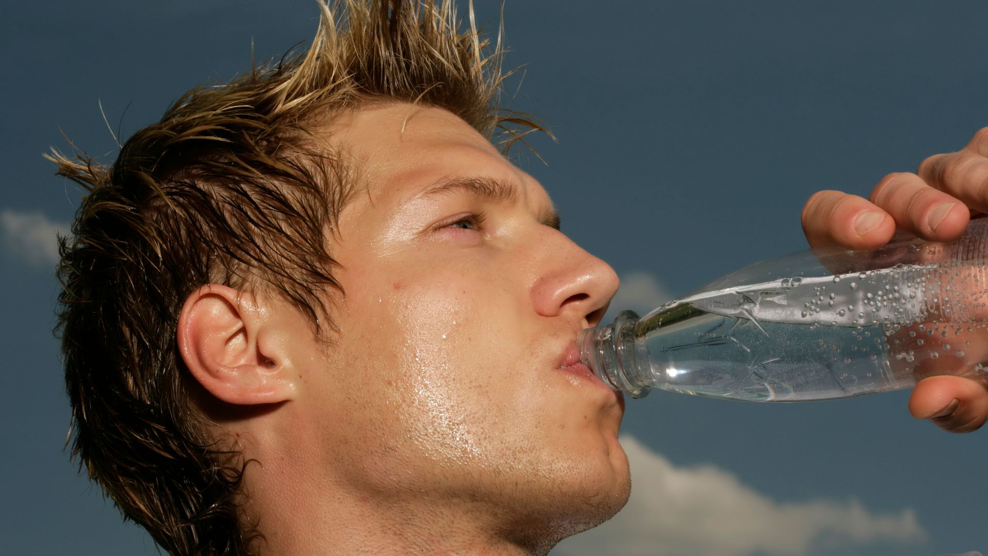 Close-up of a sweaty athletic man drinking water outdoors to cool off and stay hydrated.