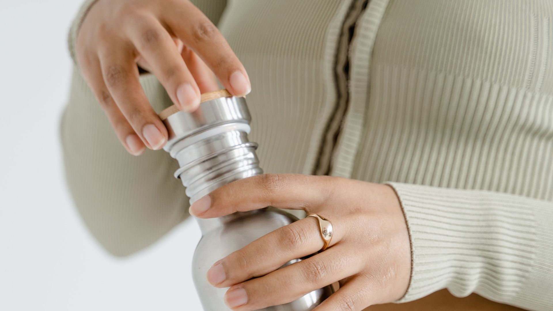 Hands twisting a reusable stainless steel bottle lid, promoting zero waste lifestyle.