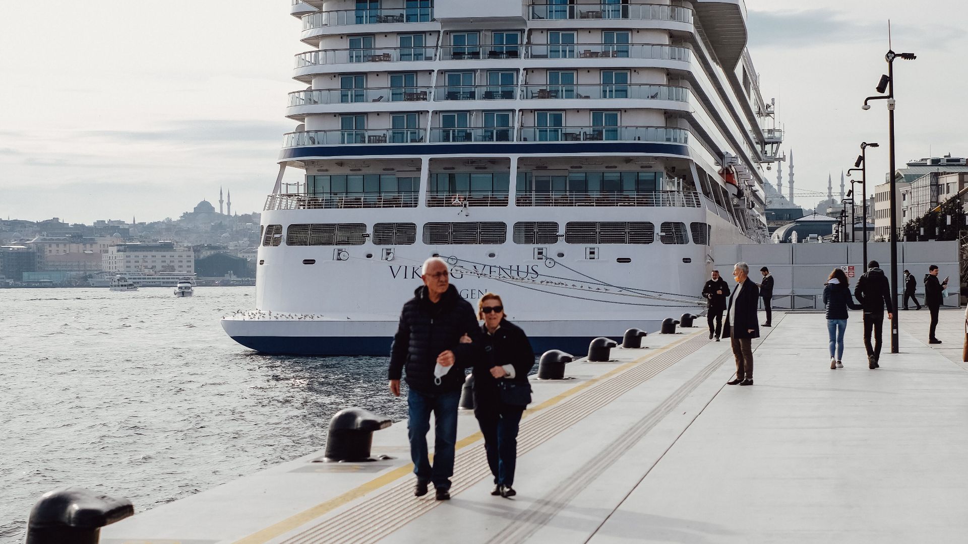 A majestic cruise ship docked at İstanbul harbor with tourists walking along the promenade.