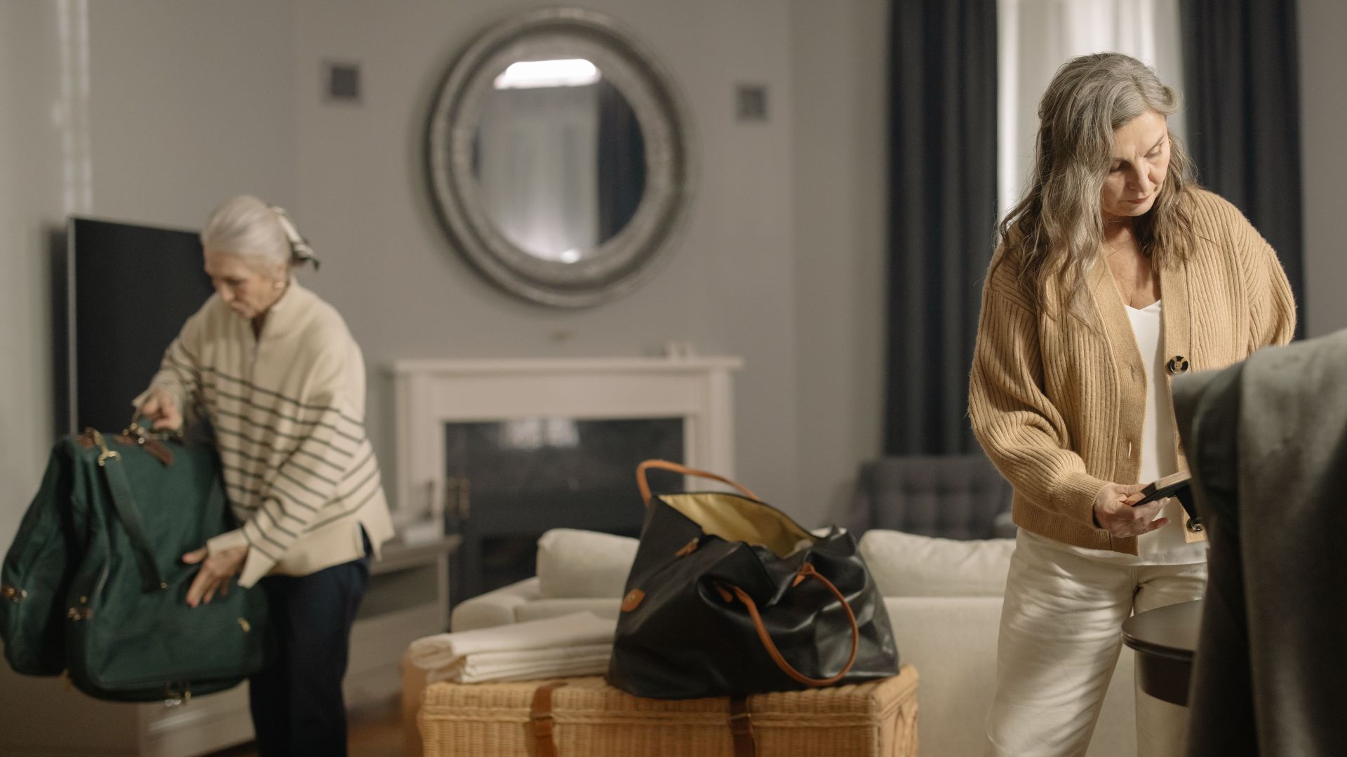 Two senior women packing belongings in a cozy living room setting.