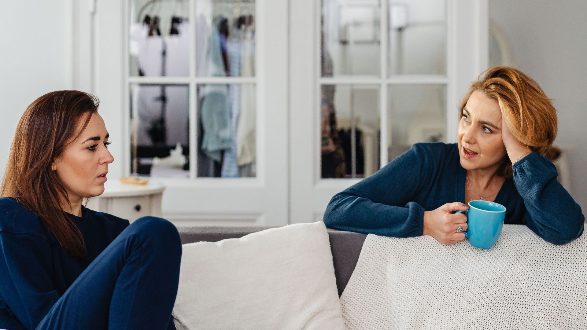 Two women having a relaxed conversation on a comfortable indoor couch.